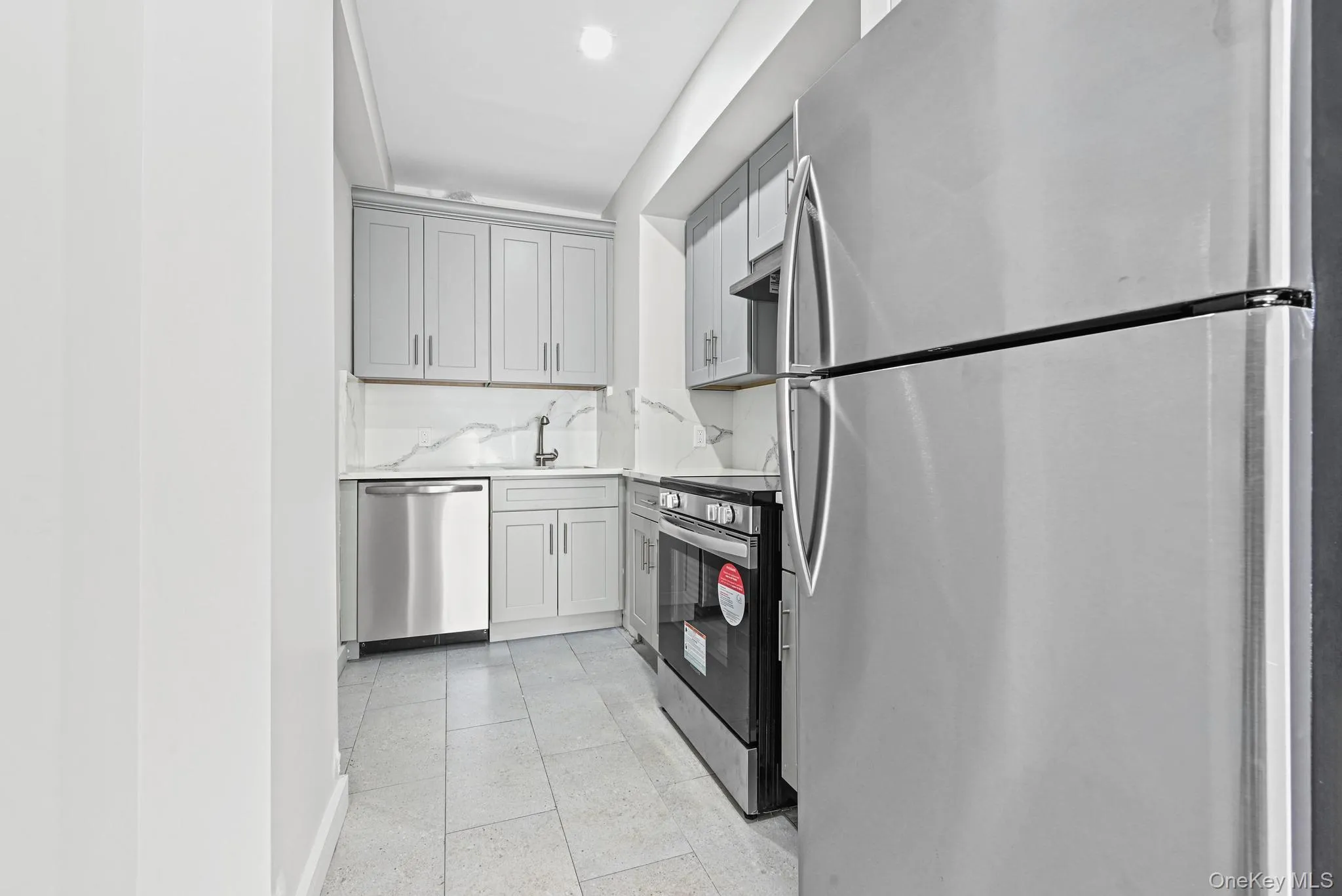 Kitchen featuring stainless steel appliances, gray cabinets, light tile patterned floors, and light stone countertops Kitchen featuring stainless steel appliances, gray cabinets, light tile patterned floors, and light stone countertops