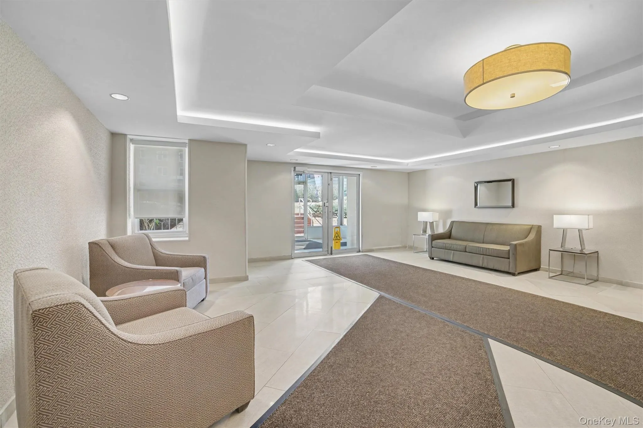 Spacious entryway featuring recessed lighting, a central oval drum light fixture, tray ceiling details, and white tile flooring complemented by a durable carpet runner Spacious entryway featuring recessed lighting, a central oval drum light fixture, tray ceiling details, and white tile flooring complemented by a durable carpet runner