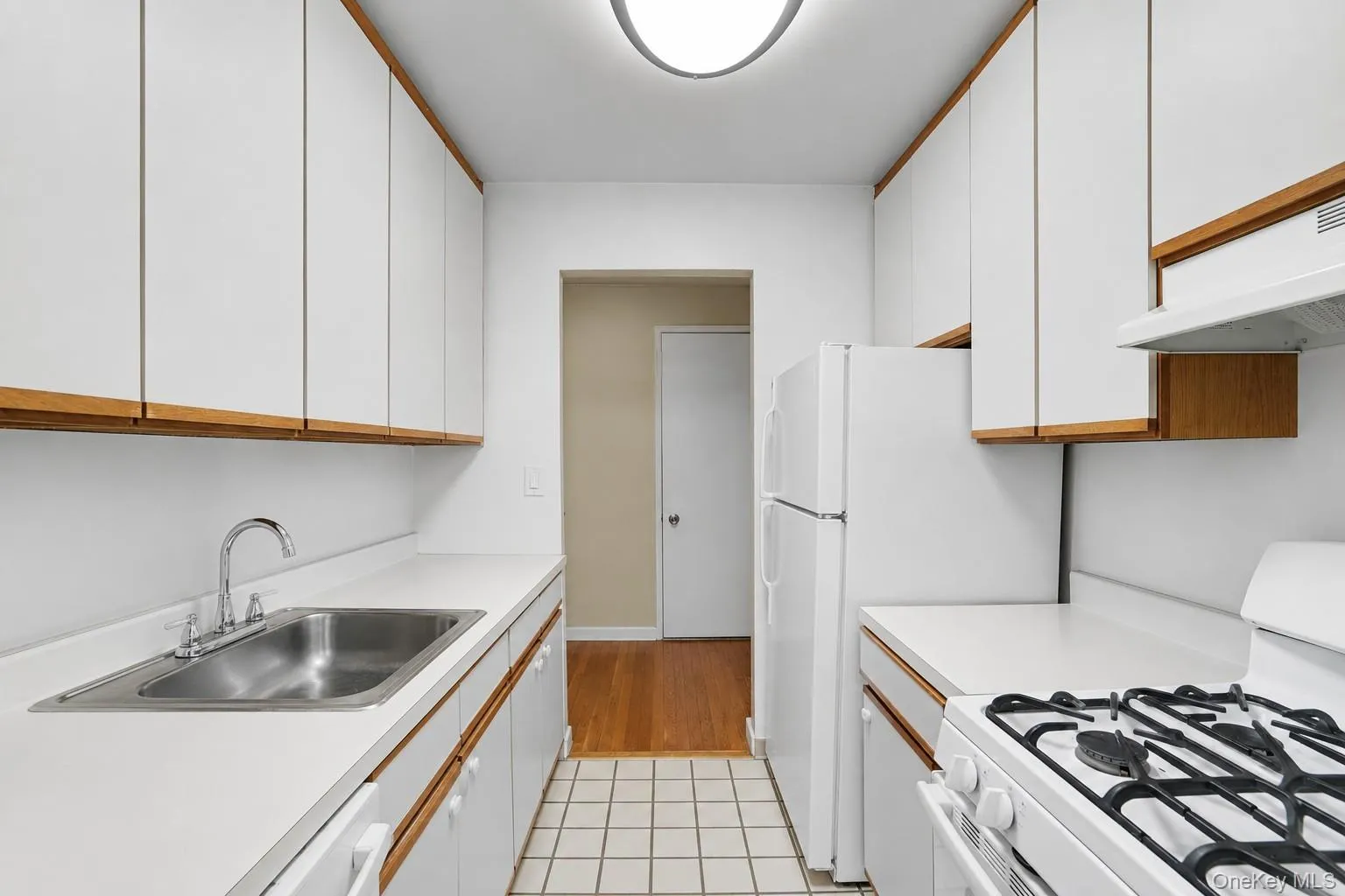 Galley kitchen featuring white cabinetry with wood trim, white countertops, a stainless steel sink, and a white gas range Galley kitchen featuring white cabinetry with wood trim, white countertops, a stainless steel sink, and a white gas range