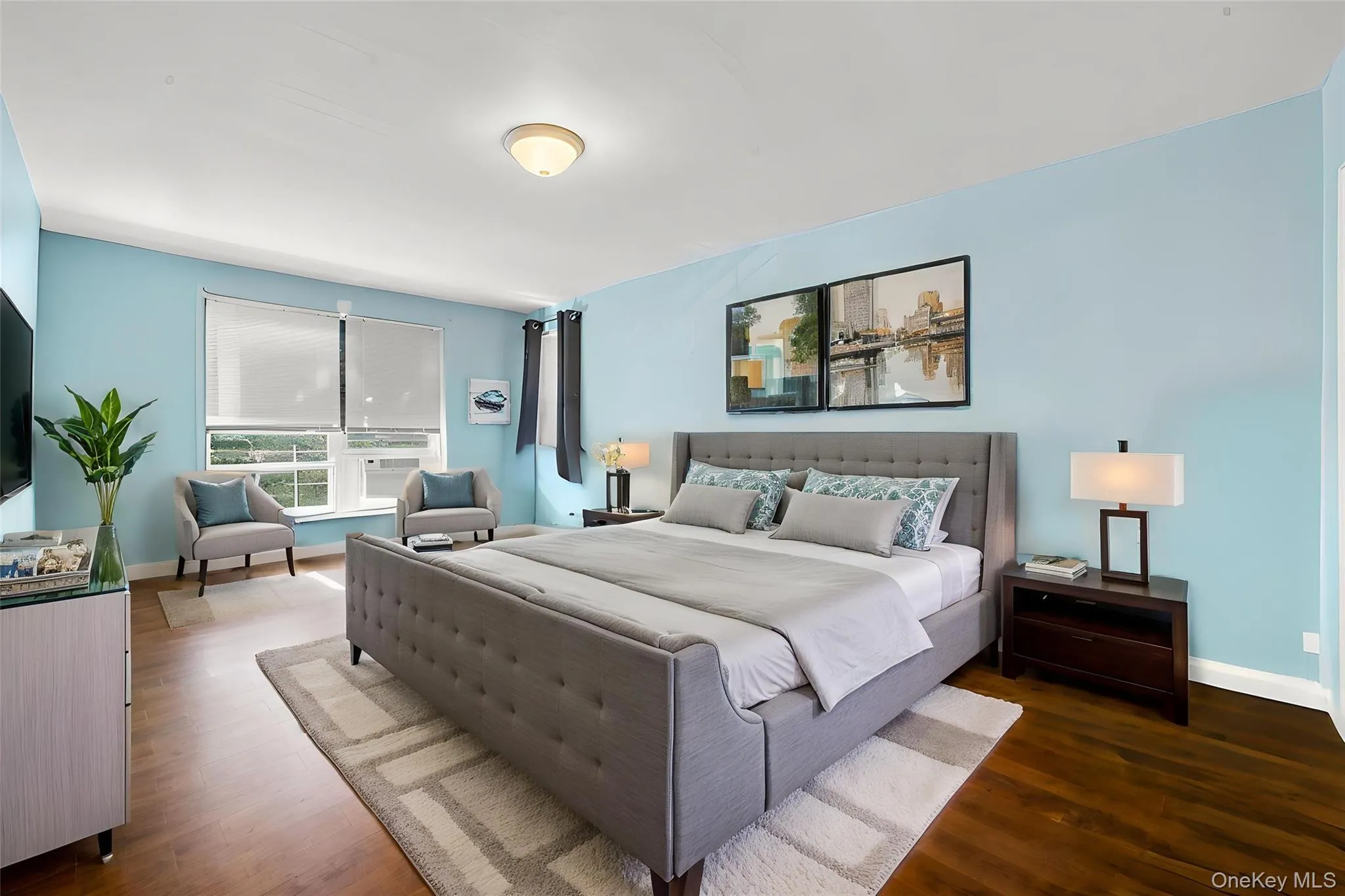 Spacious room featuring wood-finish flooring, light blue walls, and a large window with white blinds Spacious room featuring wood-finish flooring, light blue walls, and a large window with white blinds