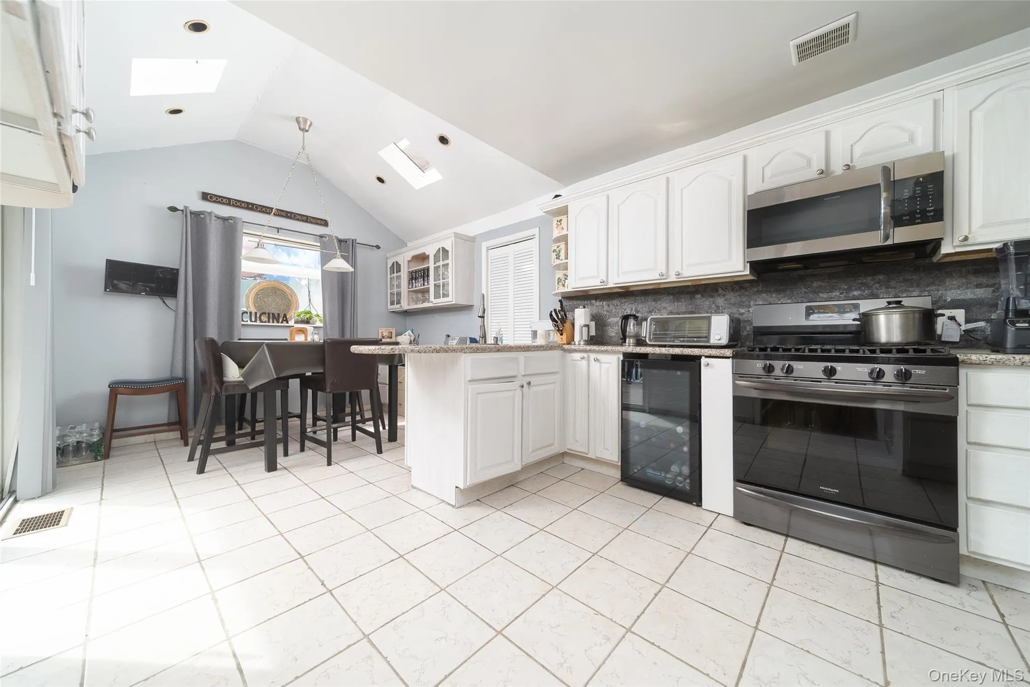 Kitchen with stainless steel appliances, a skylight, backsplash, wine cooler, and white cabinets Kitchen with stainless steel appliances, a skylight, backsplash, wine cooler, and white cabinets