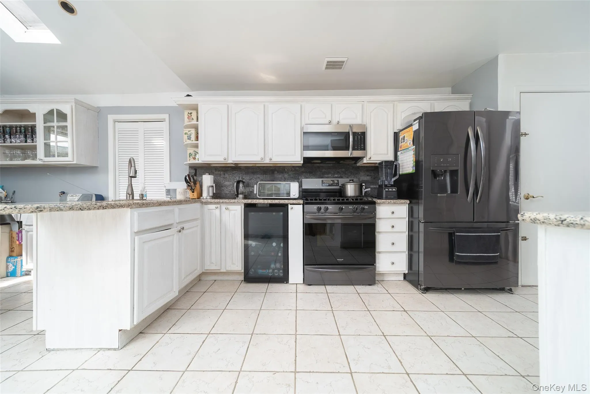 Kitchen with black fridge, light stone countertops, white cabinetry, gas stove, and open shelves Kitchen with black fridge, light stone countertops, white cabinetry, gas stove, and open shelves