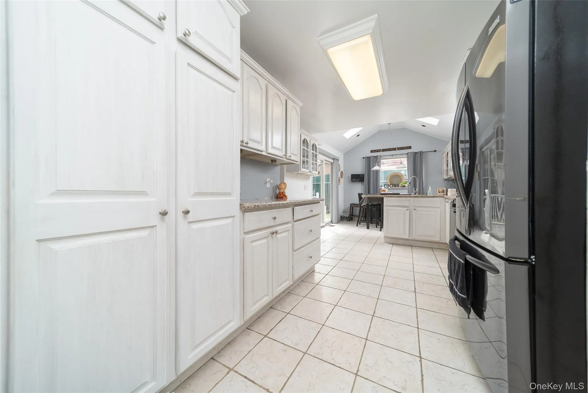 Kitchen with freestanding refrigerator, white cabinetry, light stone countertops, light tile patterned floors, and a kitchen island with sink Kitchen with freestanding refrigerator, white cabinetry, light stone countertops, light tile patterned floors, and a kitchen island with sink