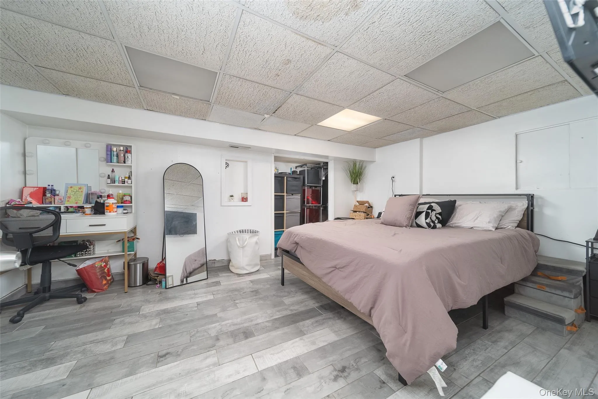 Bedroom featuring a drop ceiling, an office area, light wood-style floors, and a spacious closet Bedroom featuring a drop ceiling, an office area, light wood-style floors, and a spacious closet