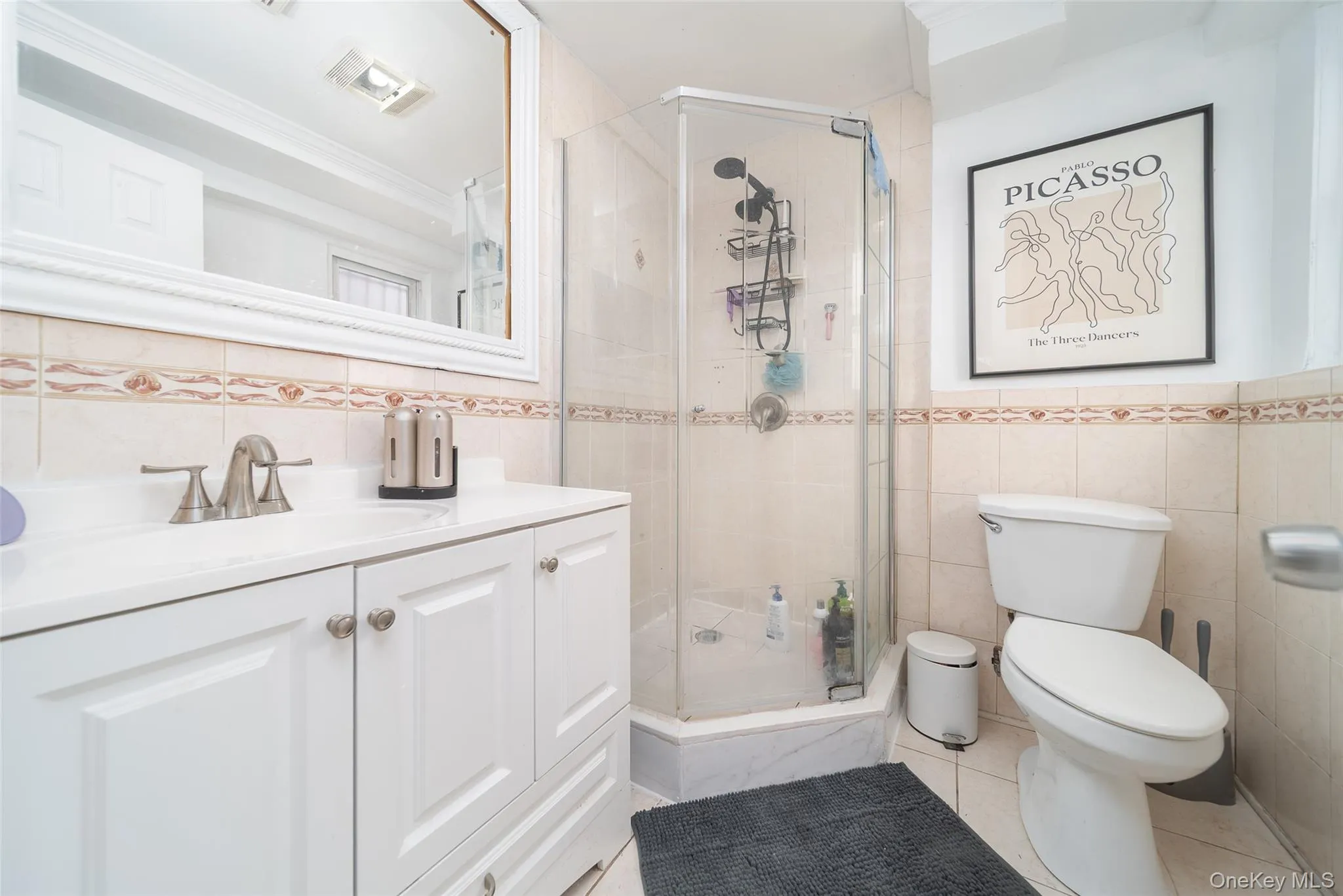 Full bath with tile walls, vanity, a shower stall, wainscoting, and light tile patterned floors Full bath with tile walls, vanity, a shower stall, wainscoting, and light tile patterned floors