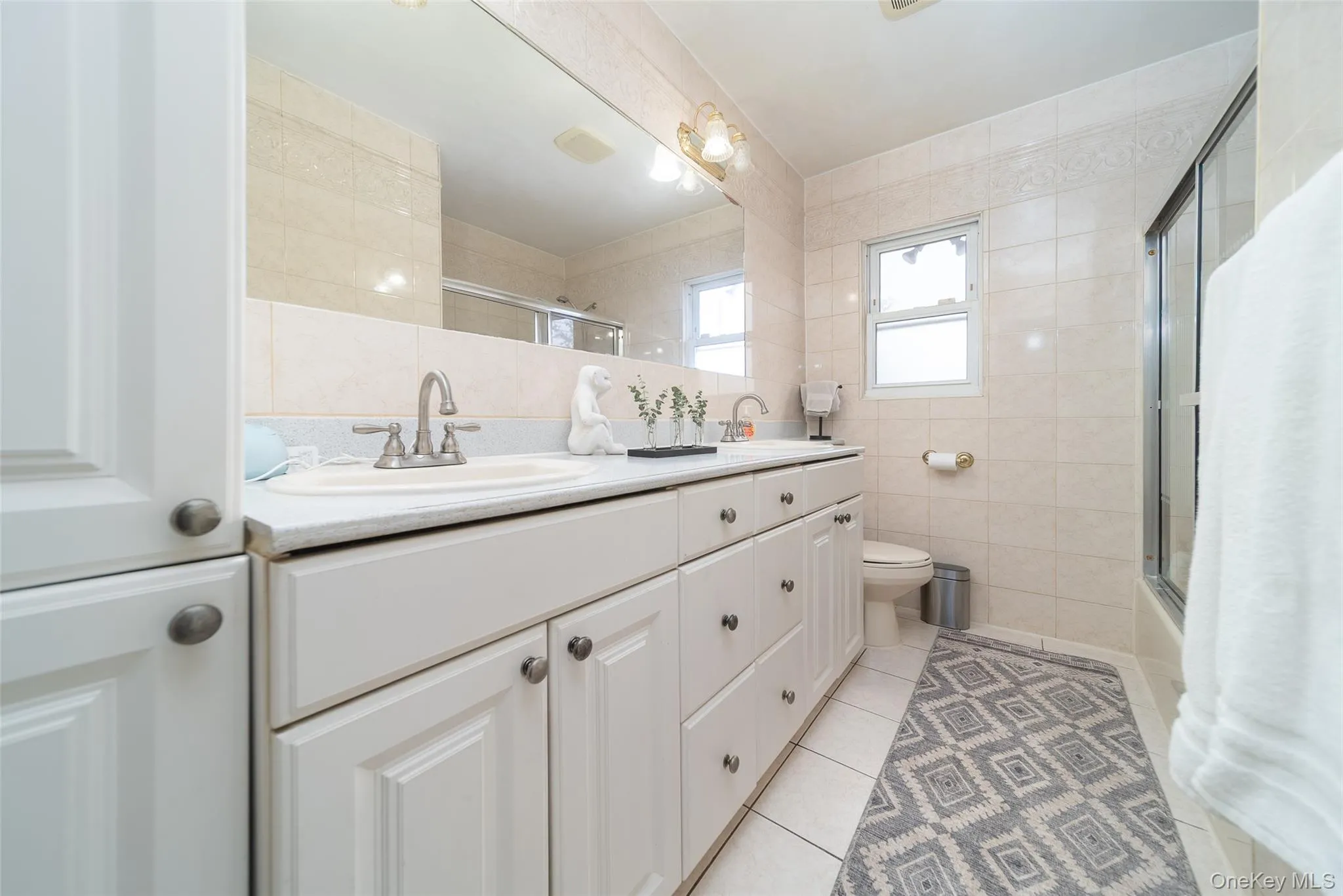 Full bath with tile walls, double vanity, light tile patterned floors, and enclosed tub / shower combo Full bath with tile walls, double vanity, light tile patterned floors, and enclosed tub / shower combo