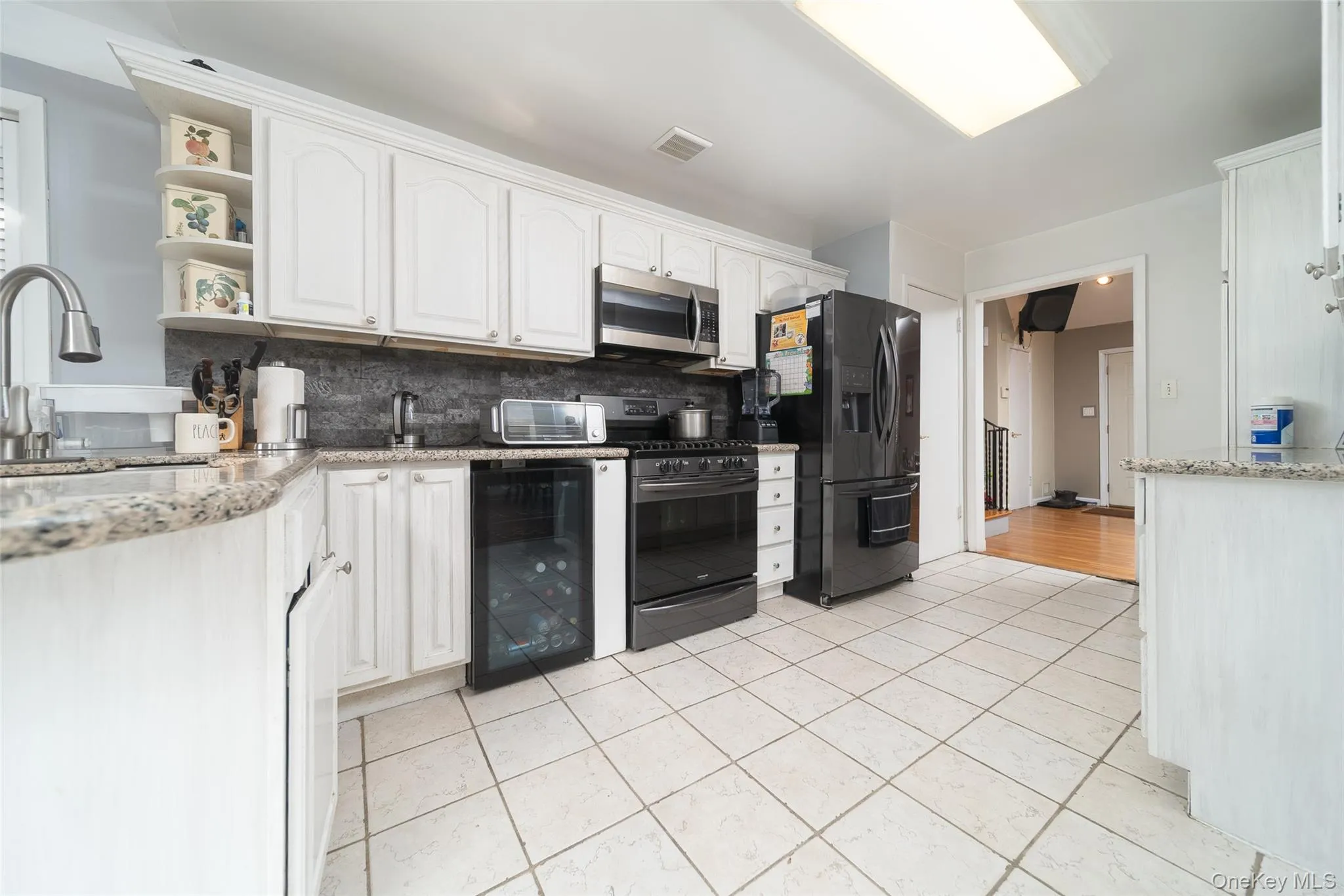Kitchen featuring light stone counters, backsplash, gas stove, white cabinetry, and black fridge with ice dispenser Kitchen featuring light stone counters, backsplash, gas stove, white cabinetry, and black fridge with ice dispenser