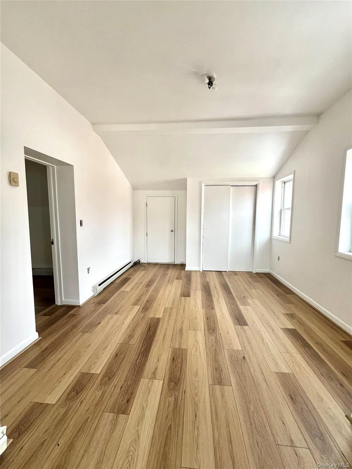 Unfurnished bedroom with vaulted ceiling with beams, light wood-type flooring, and a baseboard heating unit Unfurnished bedroom with vaulted ceiling with beams, light wood-type flooring, and a baseboard heating unit