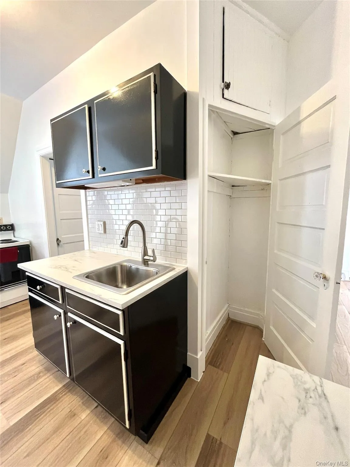 Kitchen with light countertops, light wood finished floors, range with electric cooktop, backsplash, and dark cabinets Kitchen with light countertops, light wood finished floors, range with electric cooktop, backsplash, and dark cabinets