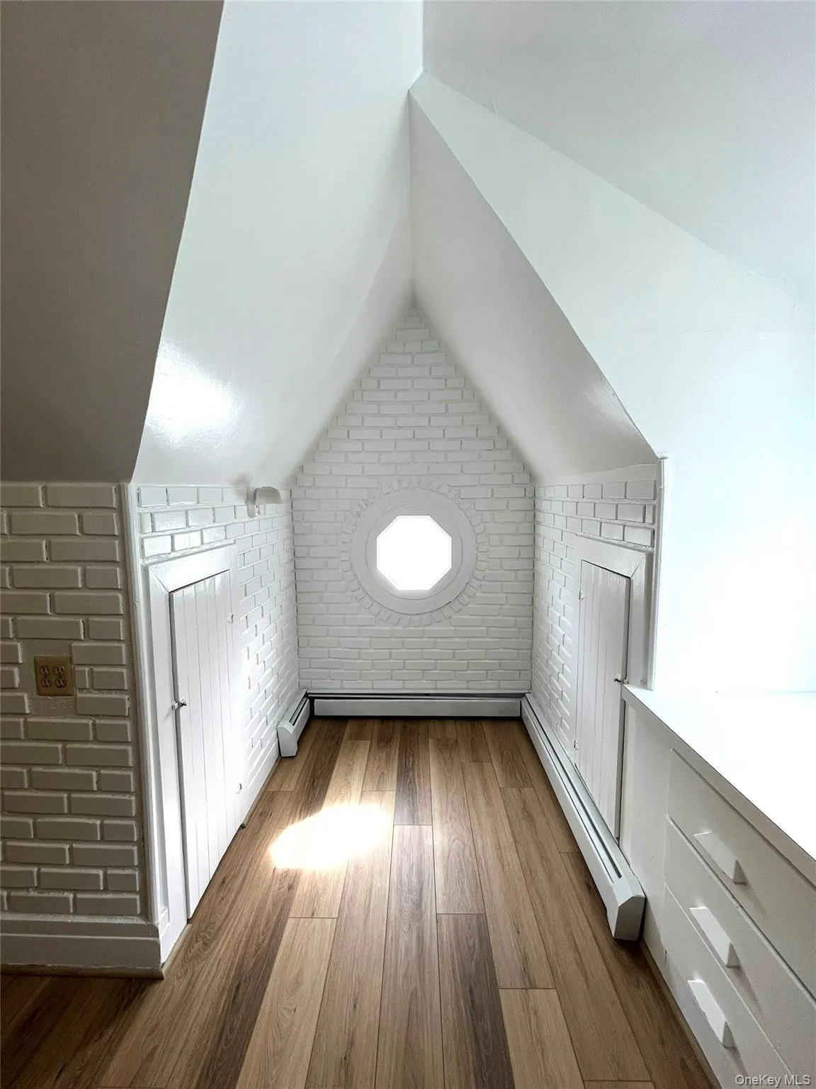 Bonus room featuring brick wall, a baseboard radiator, and dark wood-style flooring Bonus room featuring brick wall, a baseboard radiator, and dark wood-style flooring