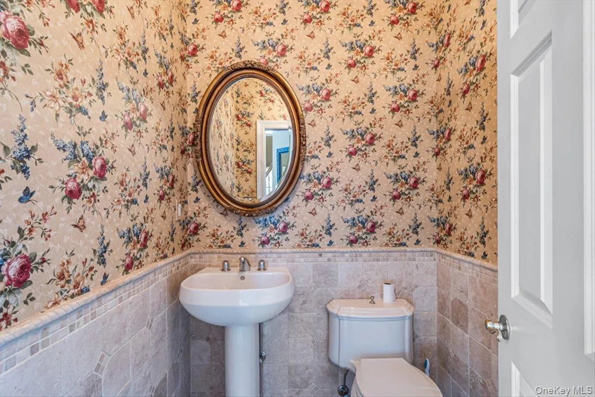 Bathroom with toilet, tile walls, wainscoting, and wallpapered walls Bathroom with toilet, tile walls, wainscoting, and wallpapered walls