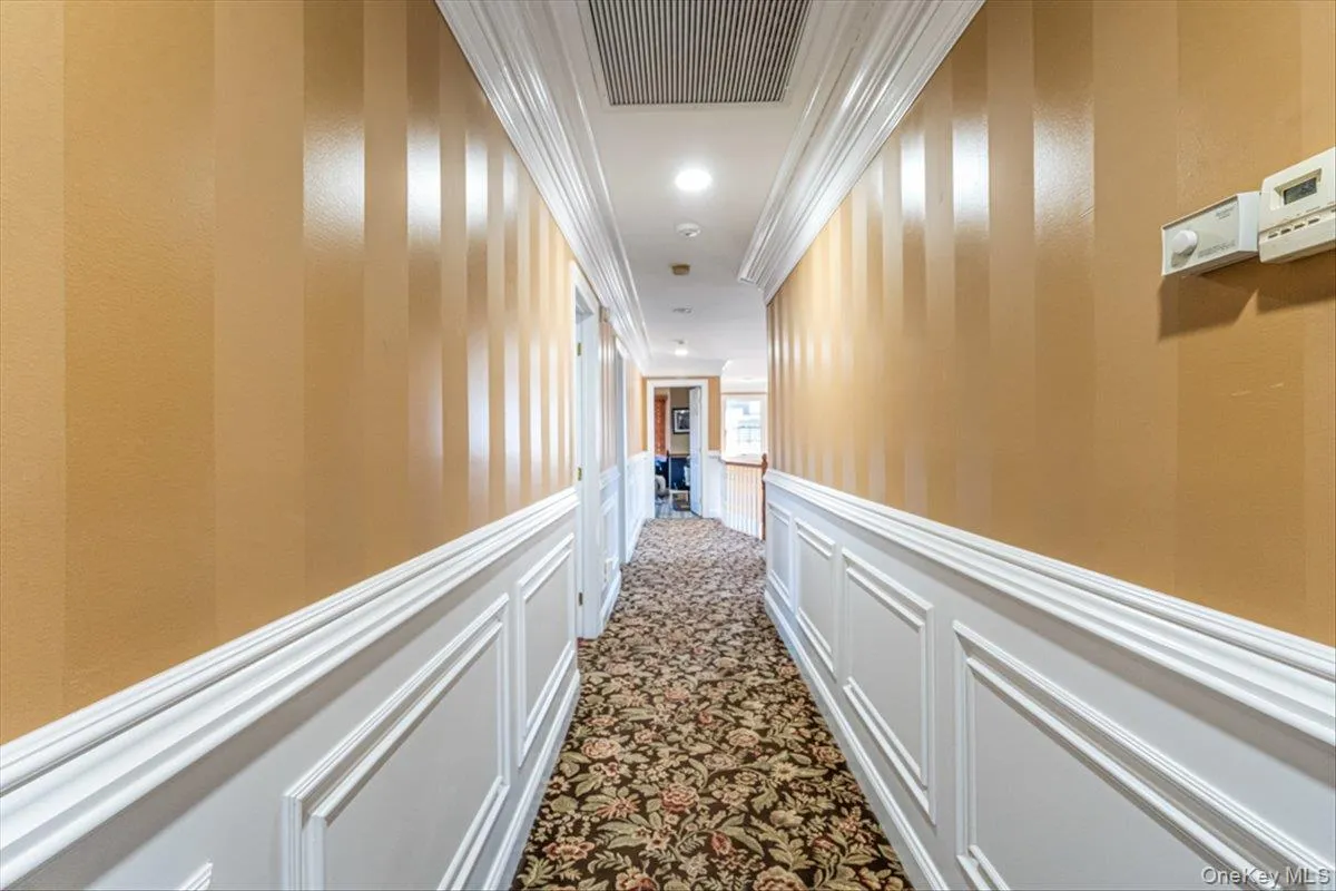 Hallway featuring visible vents, crown molding, a wainscoted wall, dark carpet, and a decorative wall Hallway featuring visible vents, crown molding, a wainscoted wall, dark carpet, and a decorative wall