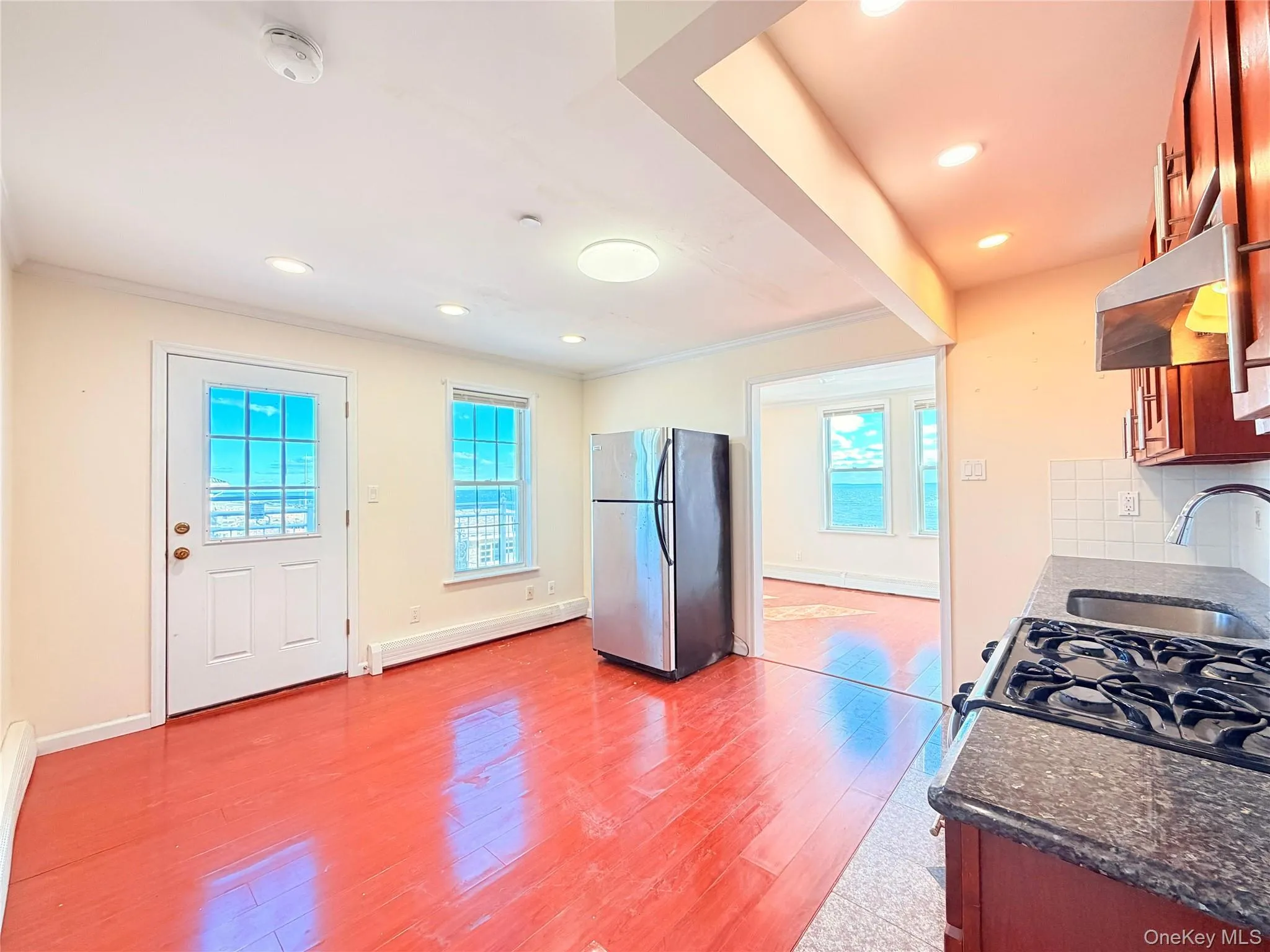 Kitchen with freestanding refrigerator, light wood-type flooring, exhaust hood, dark stone counters, and backsplash Kitchen with freestanding refrigerator, light wood-type flooring, exhaust hood, dark stone counters, and backsplash