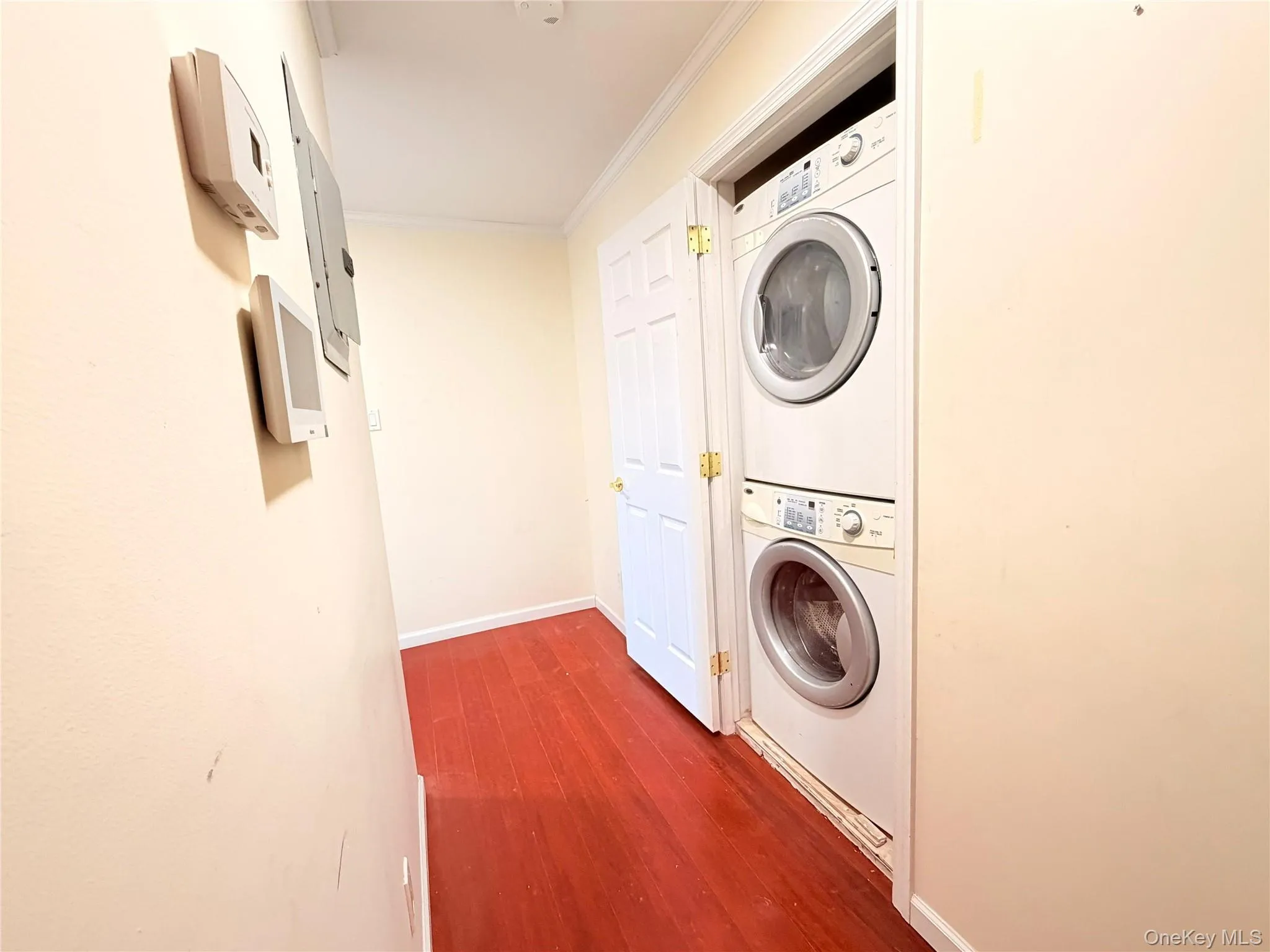 Laundry area featuring ornamental molding, dark wood-type flooring, and stacked washer / drying machine Laundry area featuring ornamental molding, dark wood-type flooring, and stacked washer / drying machine