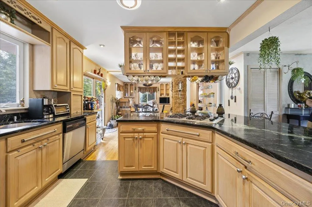 Kitchen with glass insert cabinets, dark stone counters, stainless steel appliances, dark tile patterned flooring, and ornamental molding Kitchen with glass insert cabinets, dark stone counters, stainless steel appliances, dark tile patterned flooring, and ornamental molding