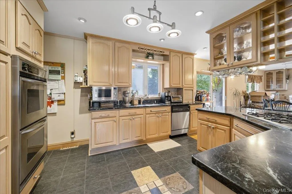 Kitchen with hanging light fixtures, stainless steel appliances, light brown cabinetry, recessed lighting, and glass insert cabinets Kitchen with hanging light fixtures, stainless steel appliances, light brown cabinetry, recessed lighting, and glass insert cabinets