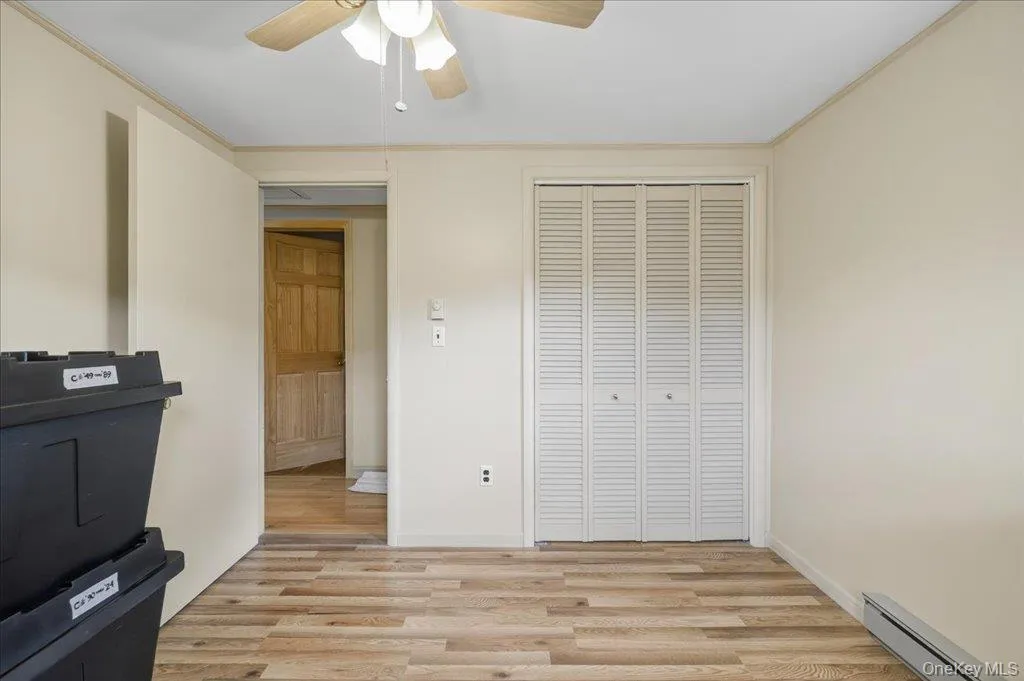 Unfurnished bedroom with light wood-style flooring, baseboard heating, a closet, crown molding, and ceiling fan Unfurnished bedroom with light wood-style flooring, baseboard heating, a closet, crown molding, and ceiling fan