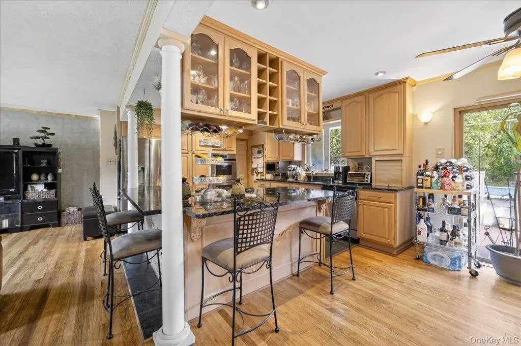Kitchen with glass insert cabinets, light wood finished floors, light brown cabinetry, a kitchen breakfast bar, and ornamental molding Kitchen with glass insert cabinets, light wood finished floors, light brown cabinetry, a kitchen breakfast bar, and ornamental molding