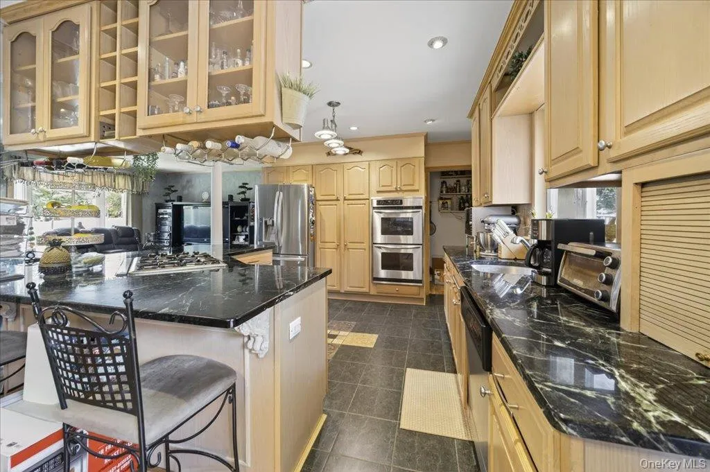 Kitchen featuring decorative light fixtures, stainless steel appliances, a kitchen breakfast bar, open floor plan, and light brown cabinets Kitchen featuring decorative light fixtures, stainless steel appliances, a kitchen breakfast bar, open floor plan, and light brown cabinets