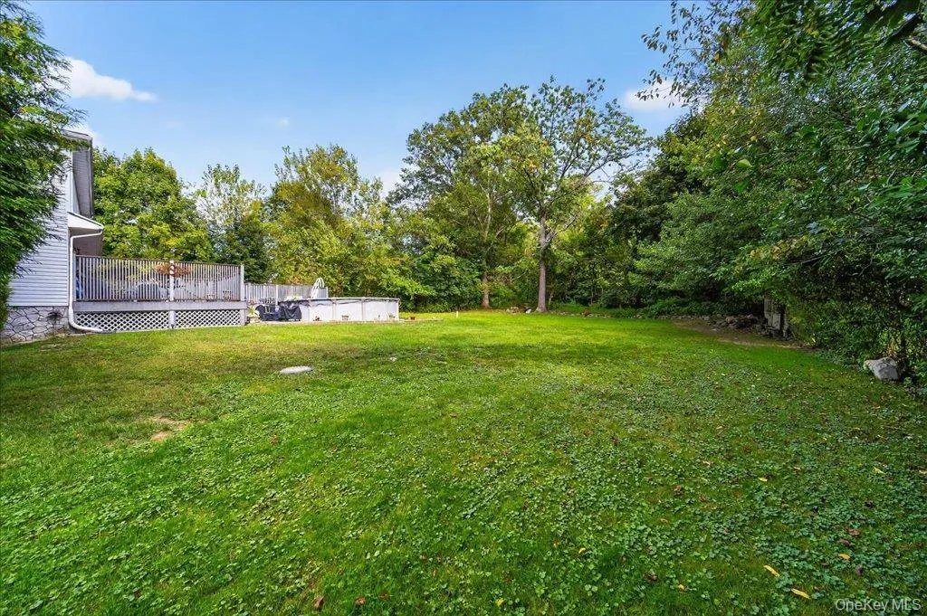 View of green lawn featuring a wooden deck, an outdoor pool, and view of scattered trees View of green lawn featuring a wooden deck, an outdoor pool, and view of scattered trees