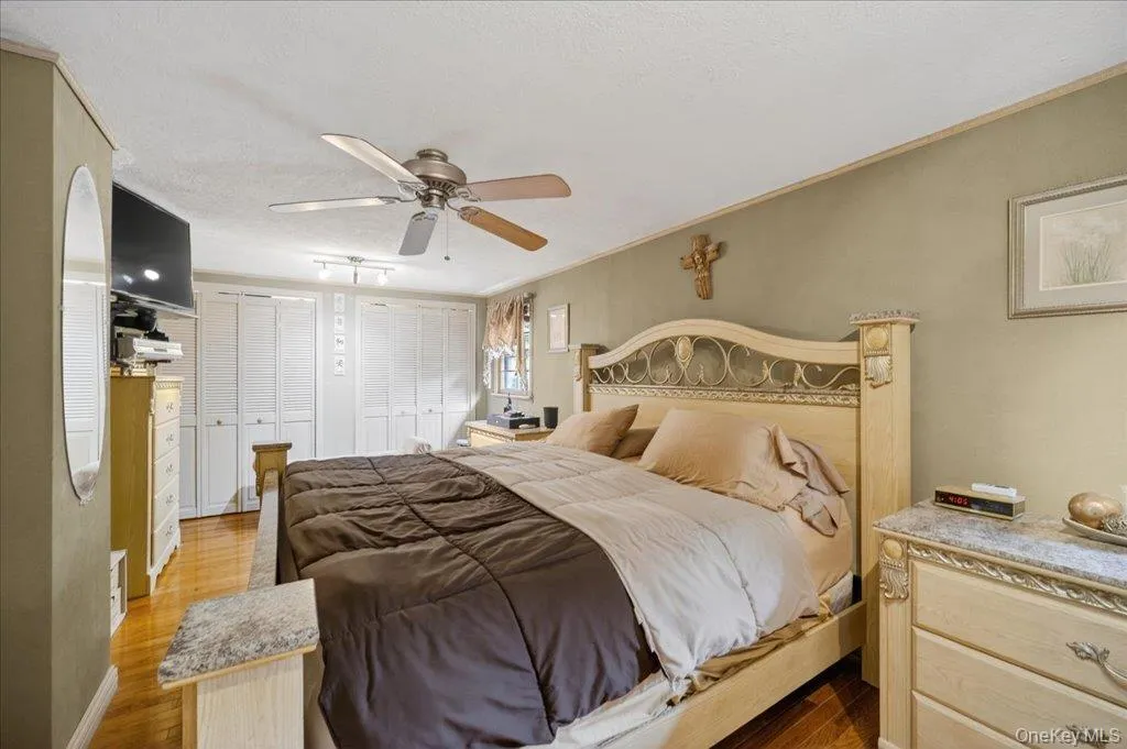 Bedroom with two closets, wood finished floors, a ceiling fan, crown molding, and a textured ceiling Bedroom with two closets, wood finished floors, a ceiling fan, crown molding, and a textured ceiling