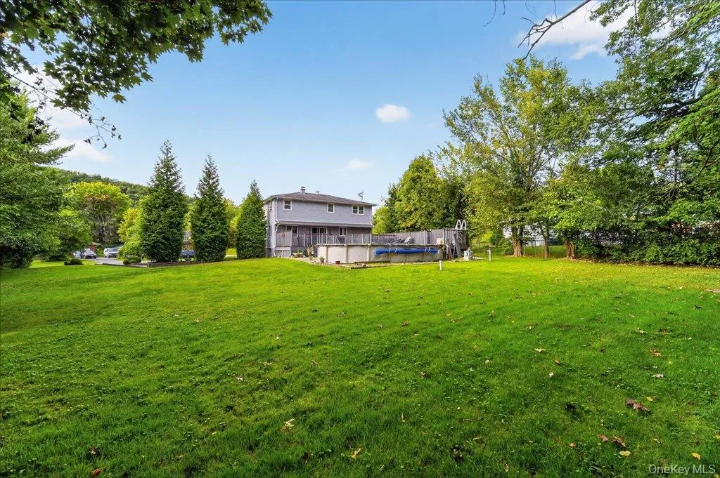 View of green lawn featuring a wooden deck, an outdoor pool, and view of scattered trees View of green lawn featuring a wooden deck, an outdoor pool, and view of scattered trees