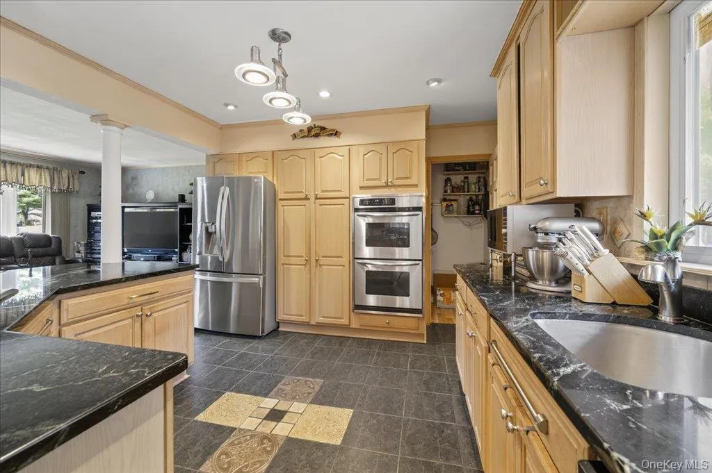 Kitchen featuring appliances with stainless steel finishes, dark stone counters, light brown cabinetry, open floor plan, and hanging light fixtures Kitchen featuring appliances with stainless steel finishes, dark stone counters, light brown cabinetry, open floor plan, and hanging light fixtures