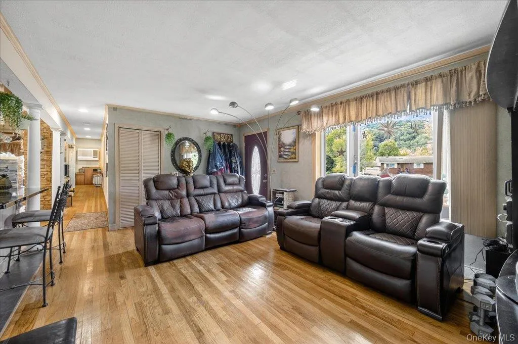 Living room featuring light wood-style flooring, crown molding, and decorative columns Living room featuring light wood-style flooring, crown molding, and decorative columns