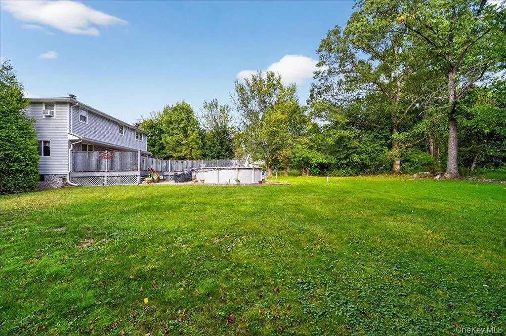 View of grassy yard featuring a deck, an outdoor pool, and view of wooded area View of grassy yard featuring a deck, an outdoor pool, and view of wooded area