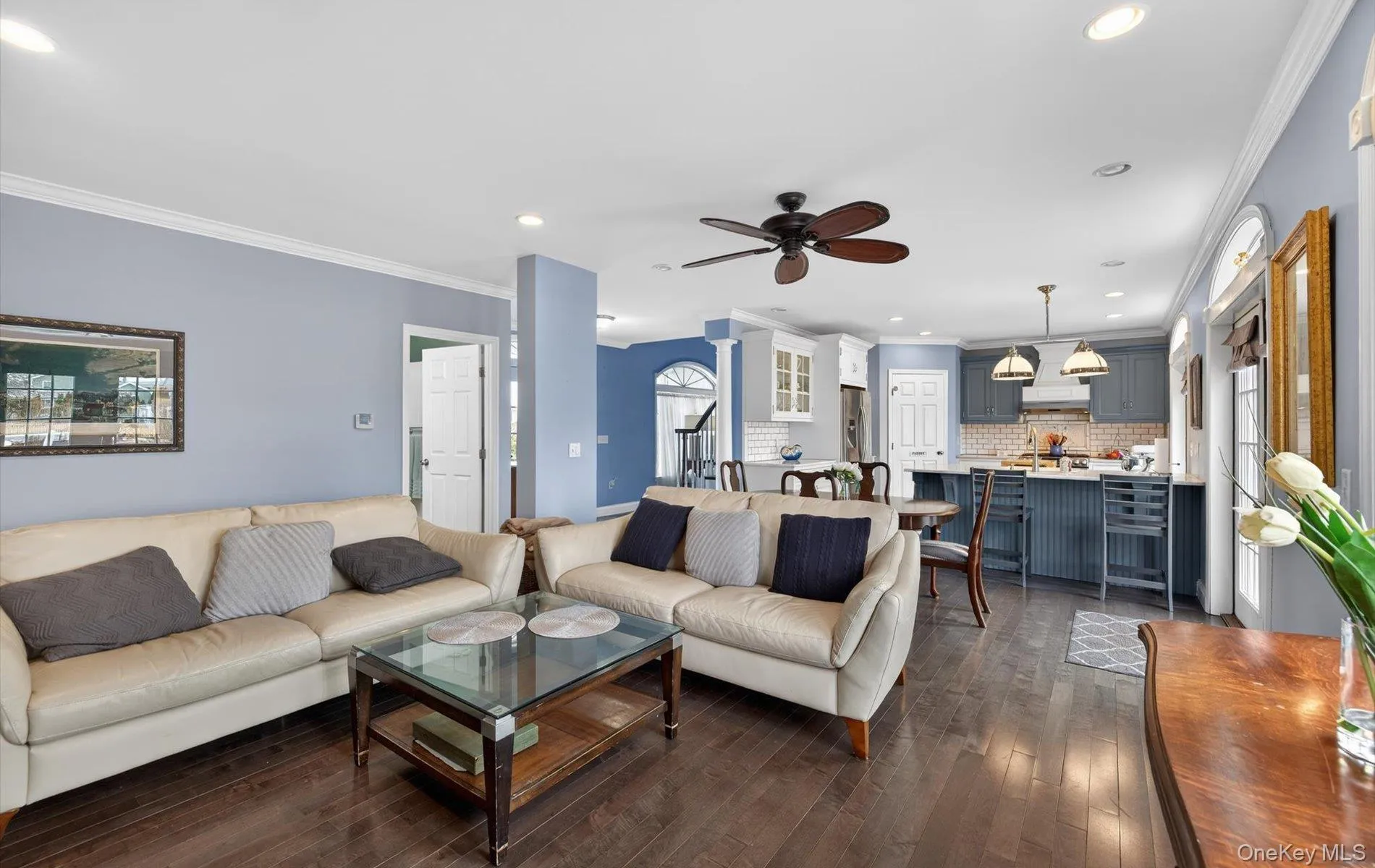 Living room featuring ornamental molding, a ceiling fan, dark wood-style flooring, recessed lighting, and decorative columns Living room featuring ornamental molding, a ceiling fan, dark wood-style flooring, recessed lighting, and decorative columns