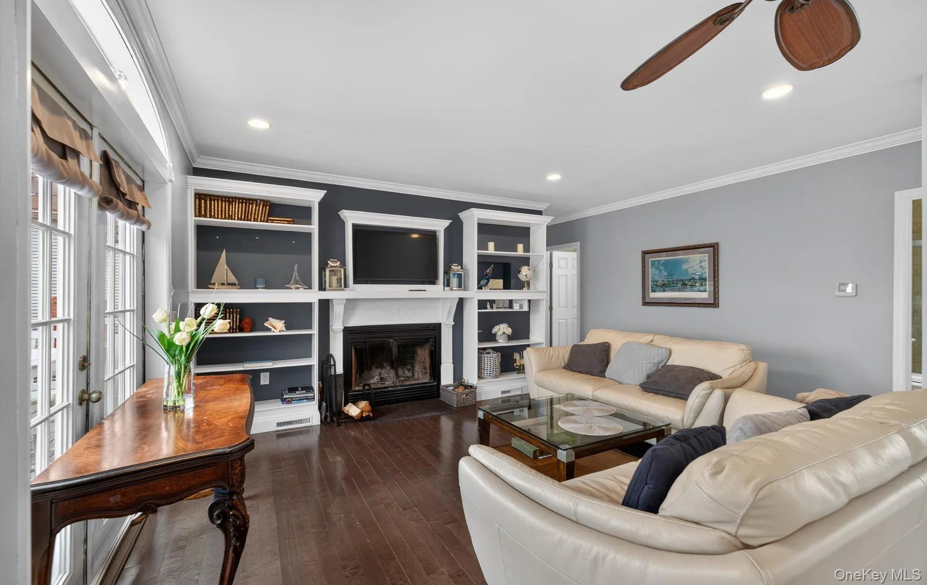 Living area with a ceiling fan, a glass covered fireplace, ornamental molding, dark wood finished floors, and built in features Living area with a ceiling fan, a glass covered fireplace, ornamental molding, dark wood finished floors, and built in features