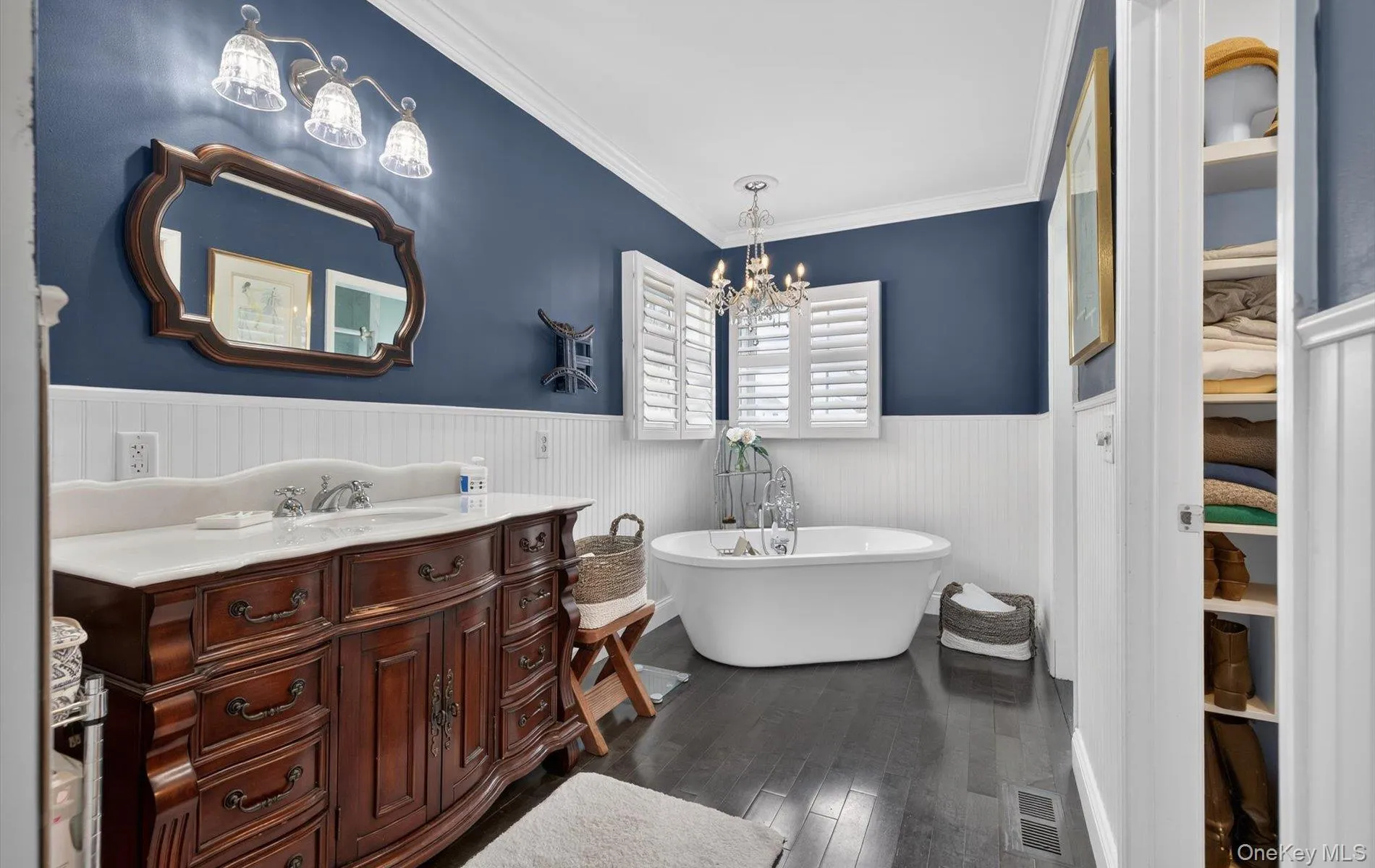 Bathroom featuring vanity, dark wood-style floors, ornamental molding, a freestanding bath, and a wainscoted wall Bathroom featuring vanity, dark wood-style floors, ornamental molding, a freestanding bath, and a wainscoted wall