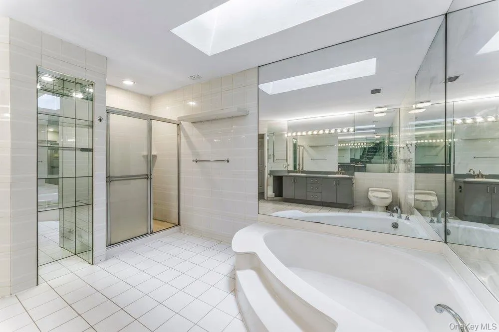 Full bathroom featuring vanity, a garden tub, a stall shower, light tile patterned flooring, and tile walls Full bathroom featuring vanity, a garden tub, a stall shower, light tile patterned flooring, and tile walls
