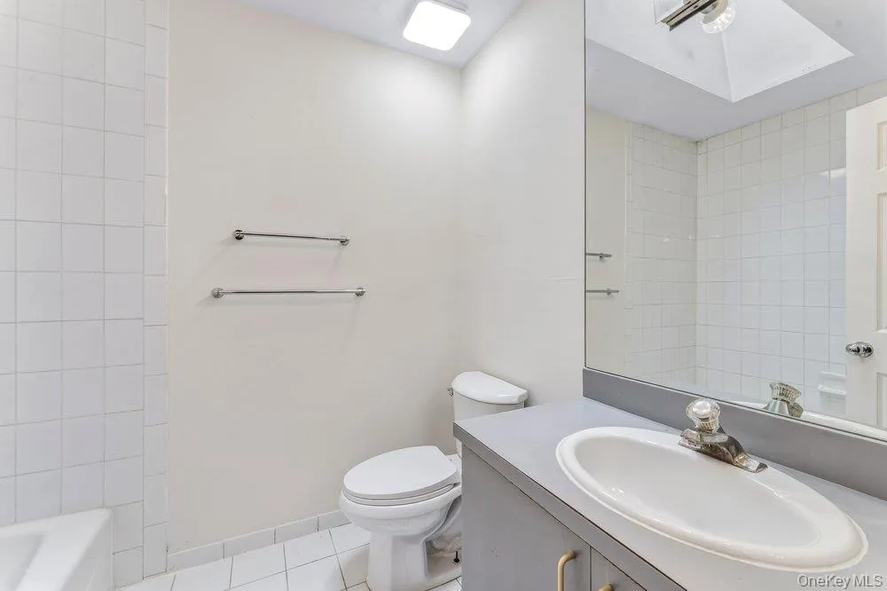 Full bathroom featuring vanity, light tile patterned floors, and a skylight Full bathroom featuring vanity, light tile patterned floors, and a skylight