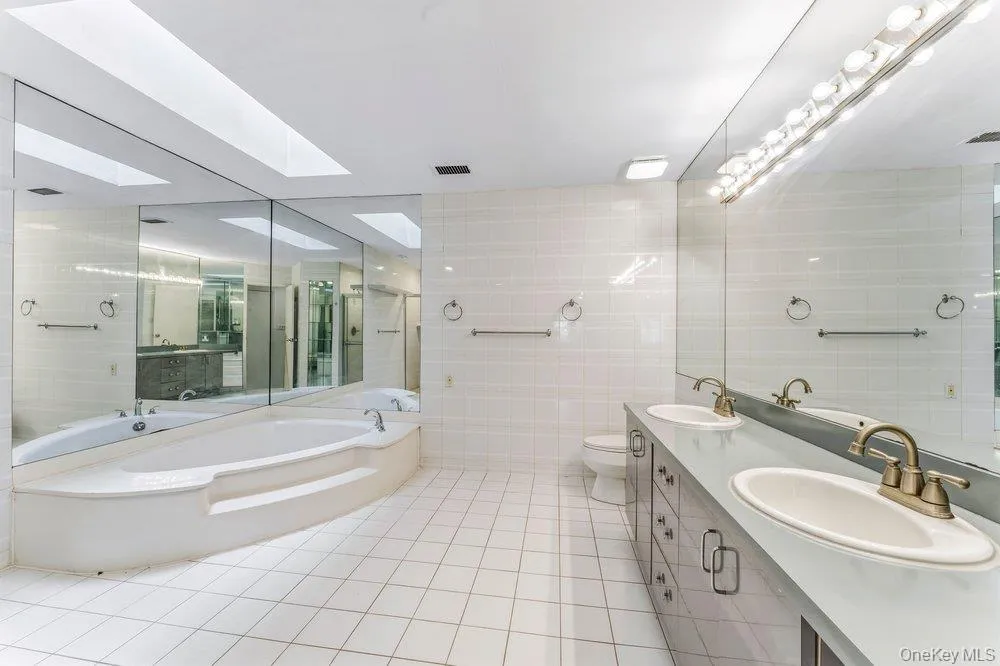 Full bathroom featuring tile walls, double vanity, a bath, and light tile patterned flooring Full bathroom featuring tile walls, double vanity, a bath, and light tile patterned flooring