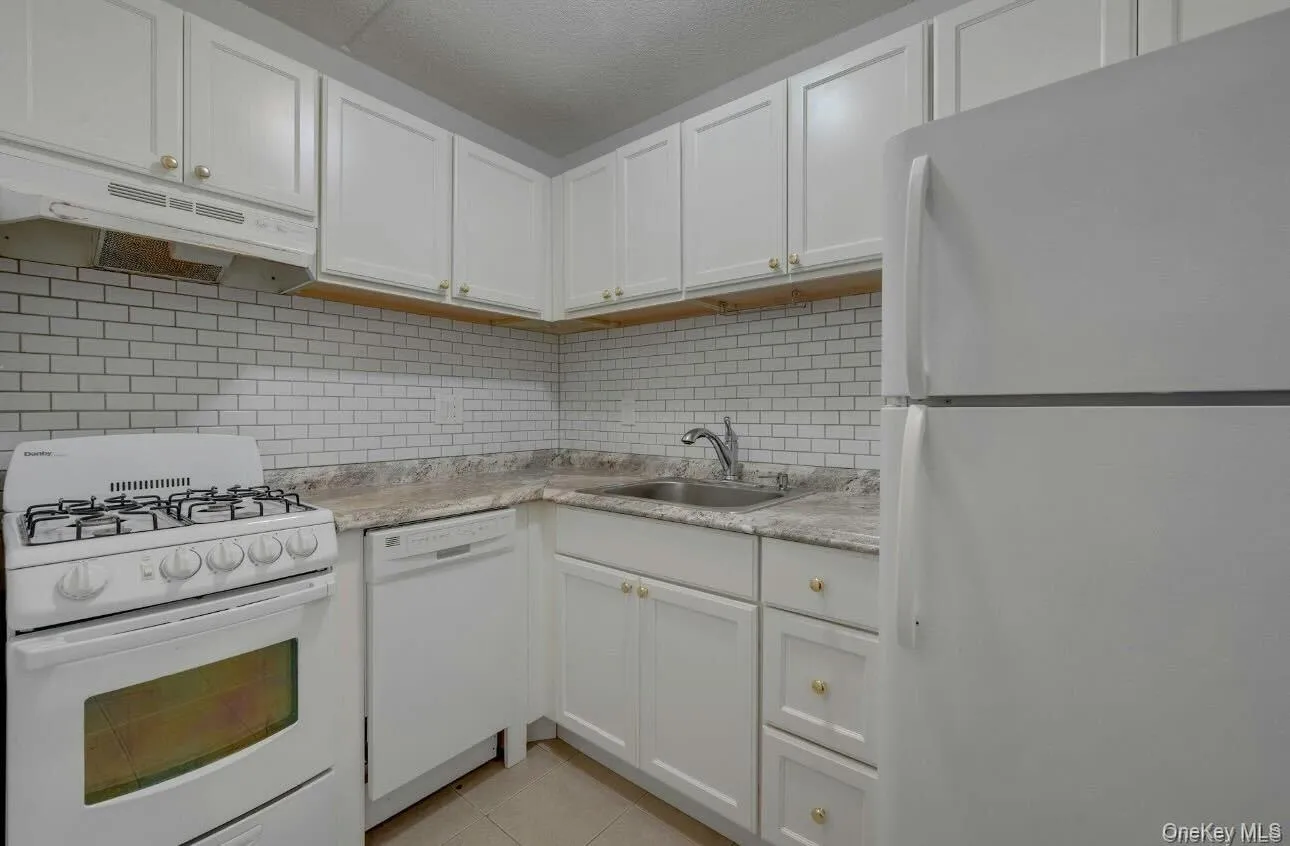 Kitchen with white appliances, light countertops, white cabinetry, tasteful backsplash, and light tile patterned floors Kitchen with white appliances, light countertops, white cabinetry, tasteful backsplash, and light tile patterned floors