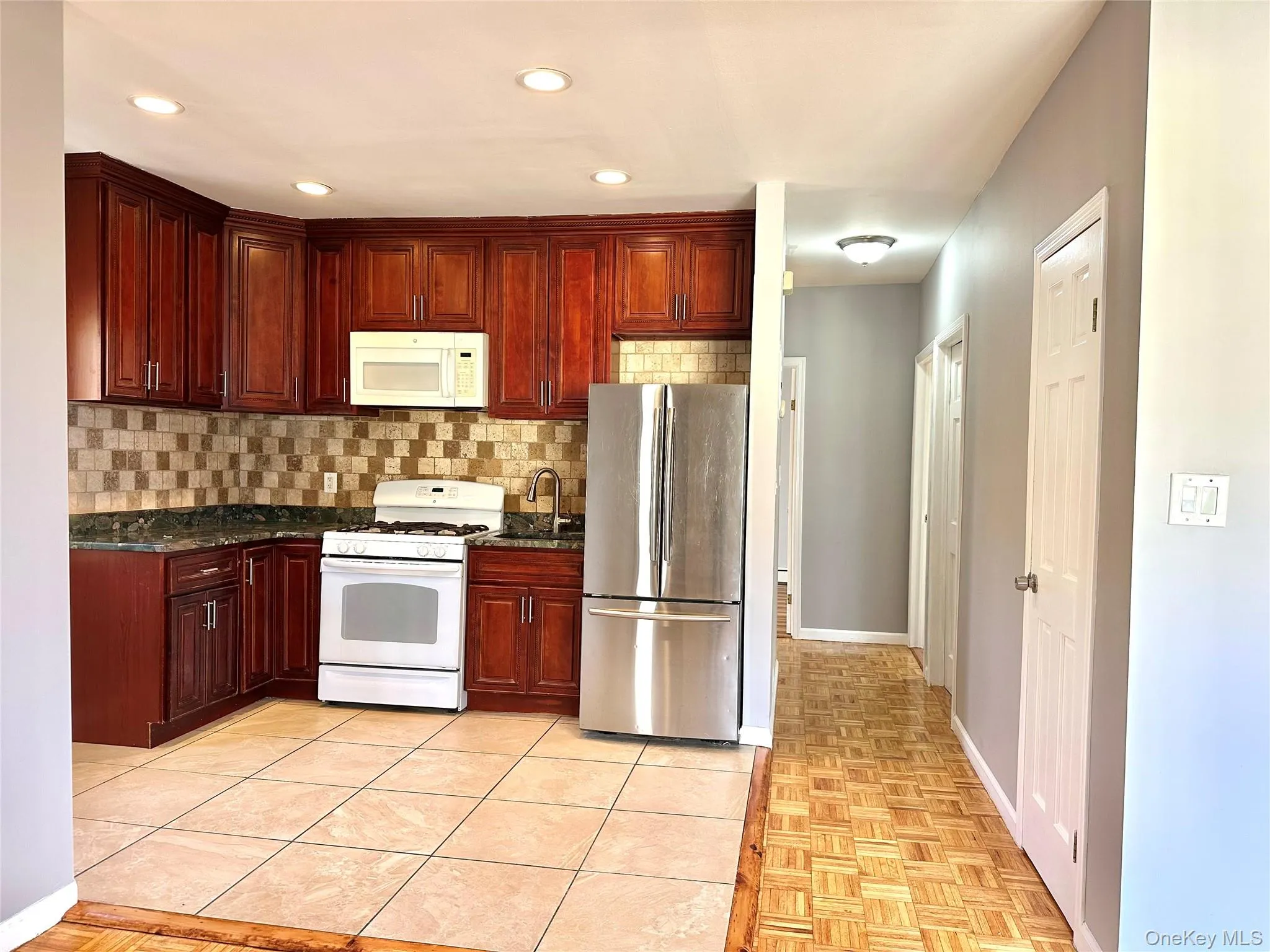 Kitchen with white appliances, dark stone countertops, recessed lighting, decorative backsplash, and reddish brown cabinets Kitchen with white appliances, dark stone countertops, recessed lighting, decorative backsplash, and reddish brown cabinets
