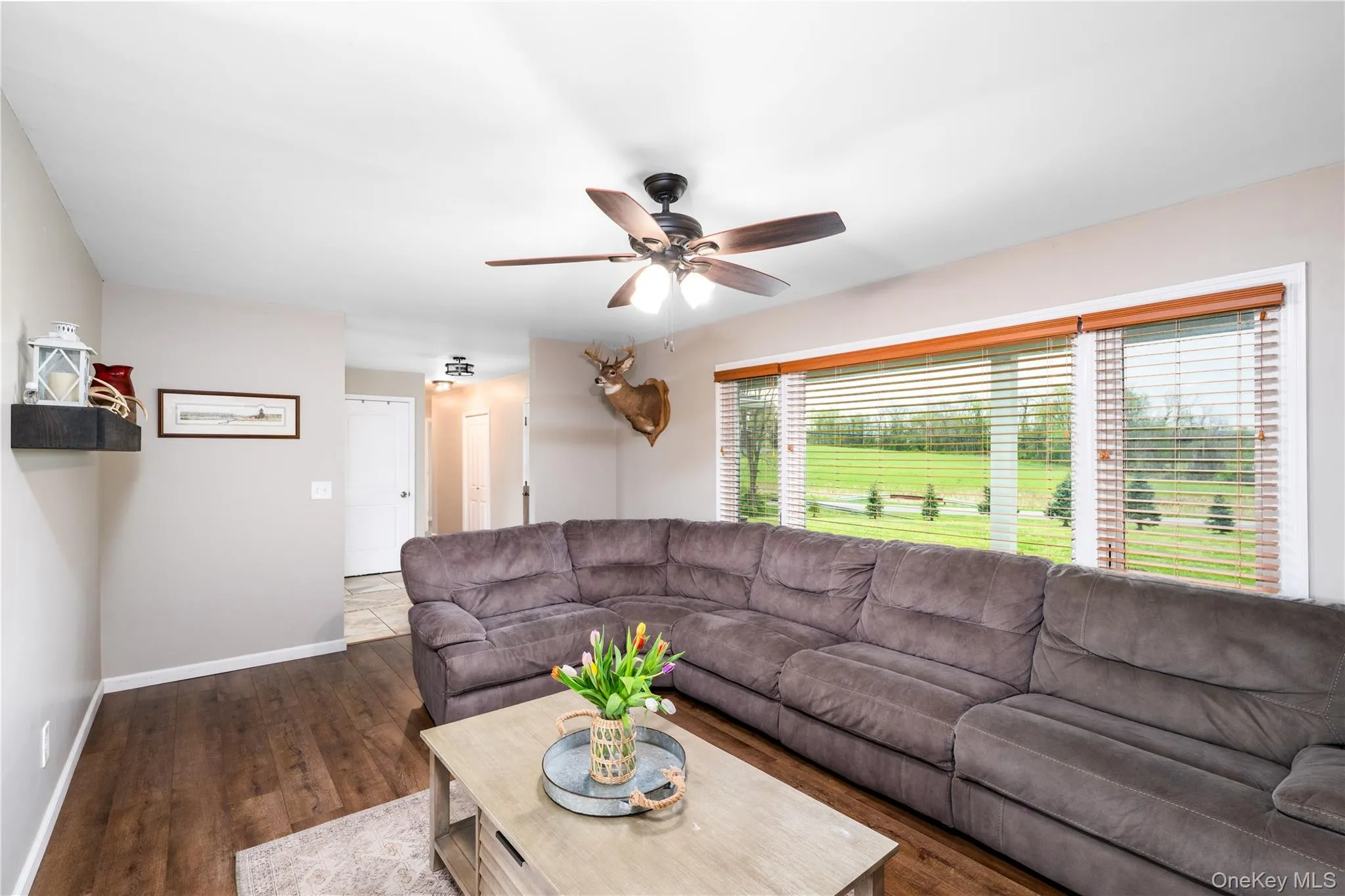Spacious living area featuring wood flooring, a ceiling fan with integrated lighting, and neutral wall tones Spacious living area featuring wood flooring, a ceiling fan with integrated lighting, and neutral wall tones