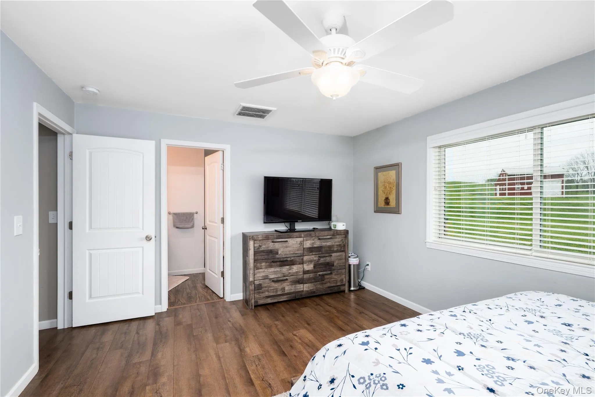 Spacious room featuring wood-flooring, a ceiling fan with light fixture, and a large window with blinds Spacious room featuring wood-flooring, a ceiling fan with light fixture, and a large window with blinds