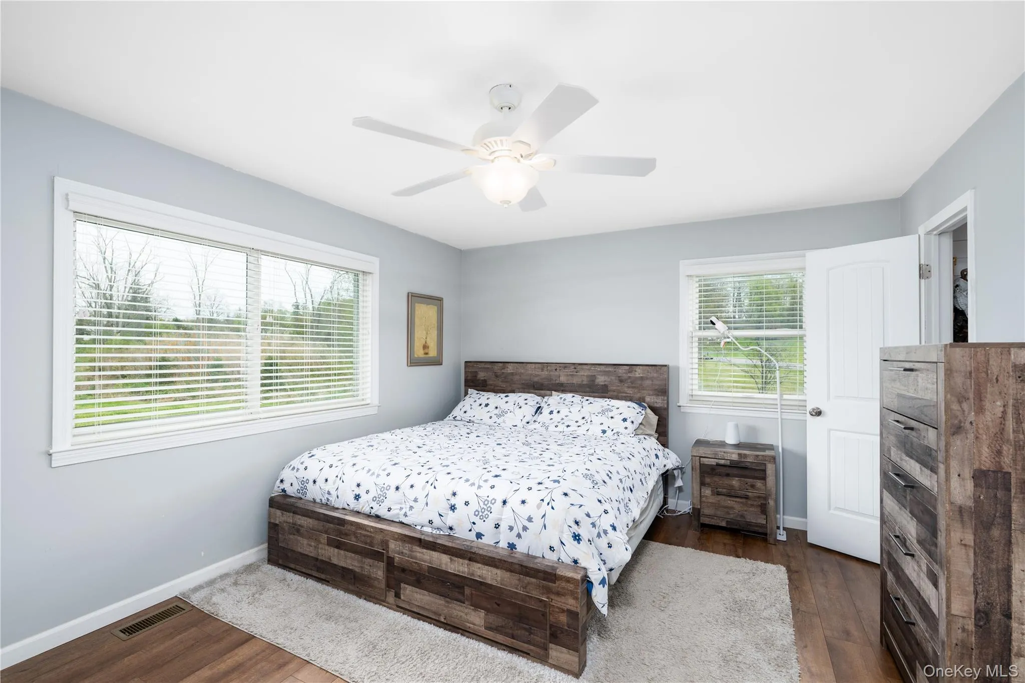 Spacious bedroom featuring light blue walls, wood flooring, and a white ceiling fan Spacious bedroom featuring light blue walls, wood flooring, and a white ceiling fan