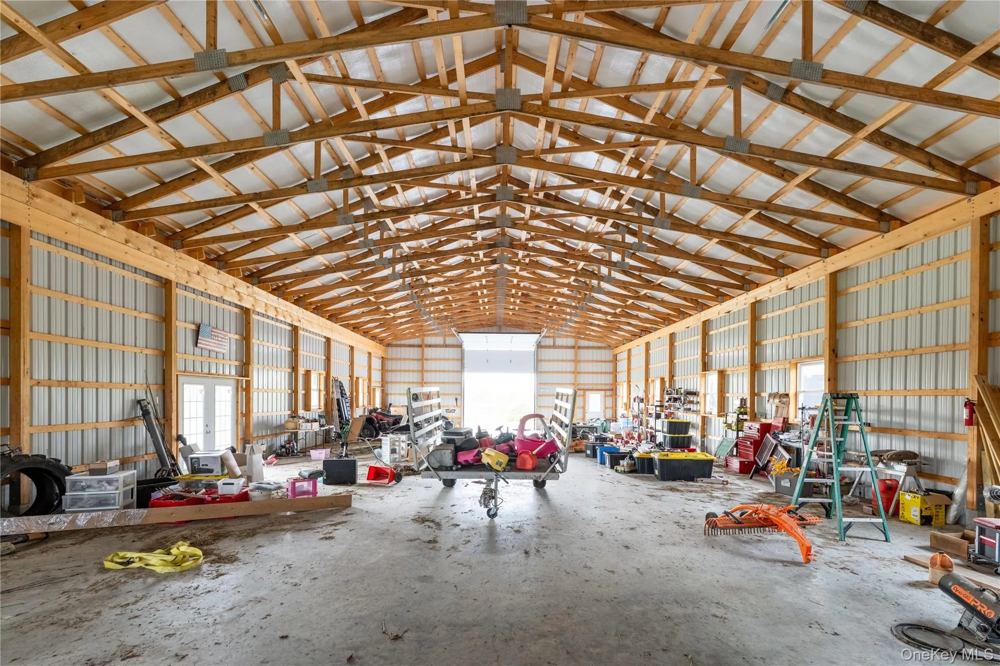 Spacious interior featuring exposed wood beam ceiling, concrete flooring, corrugated metal walls, multiple windows, and a large roll-up door Spacious interior featuring exposed wood beam ceiling, concrete flooring, corrugated metal walls, multiple windows, and a large roll-up door