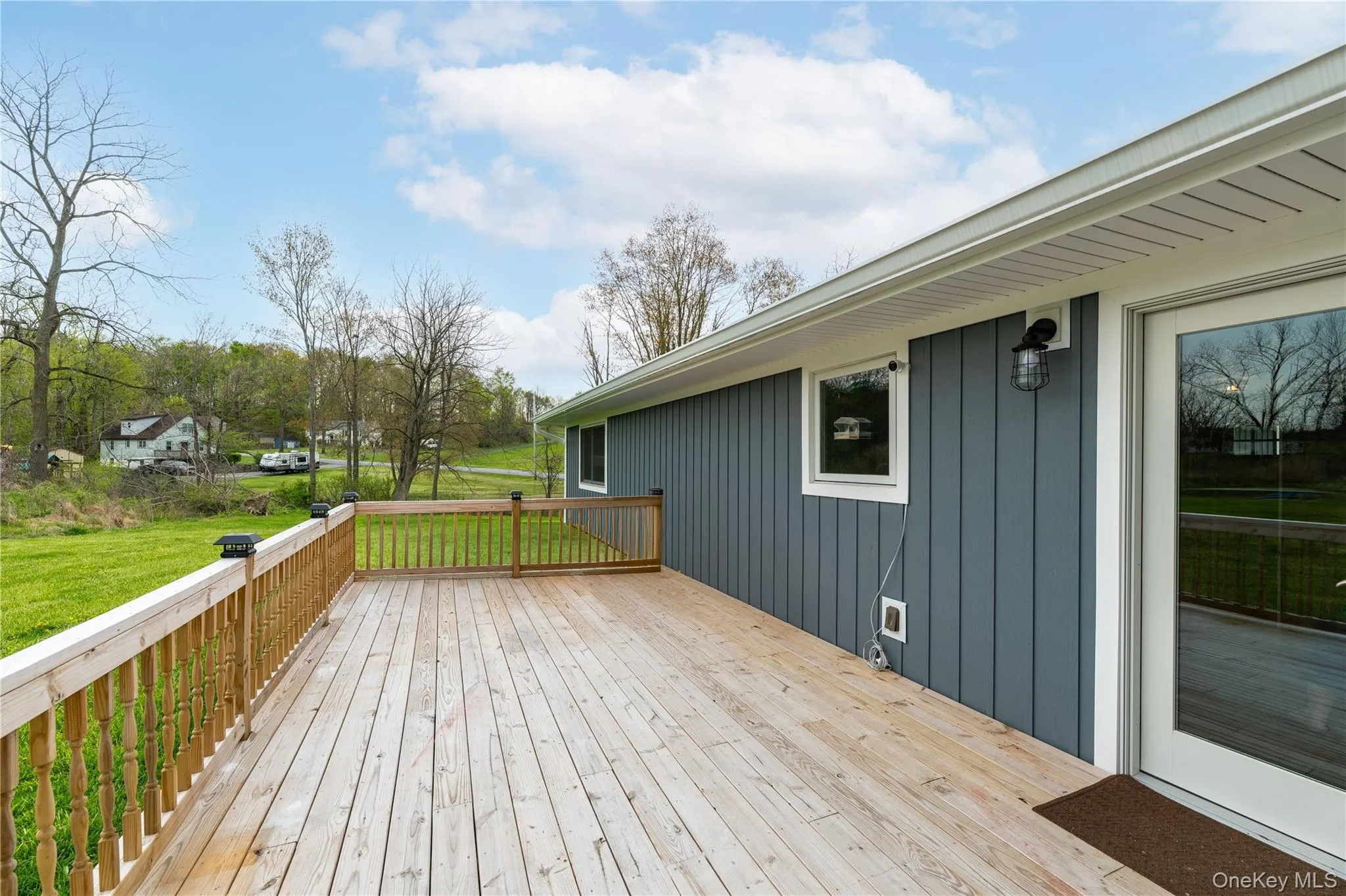 Expansive wood deck with a natural finish, featuring a wood railing with balusters, and a glass-paneled door for outdoor access Expansive wood deck with a natural finish, featuring a wood railing with balusters, and a glass-paneled door for outdoor access