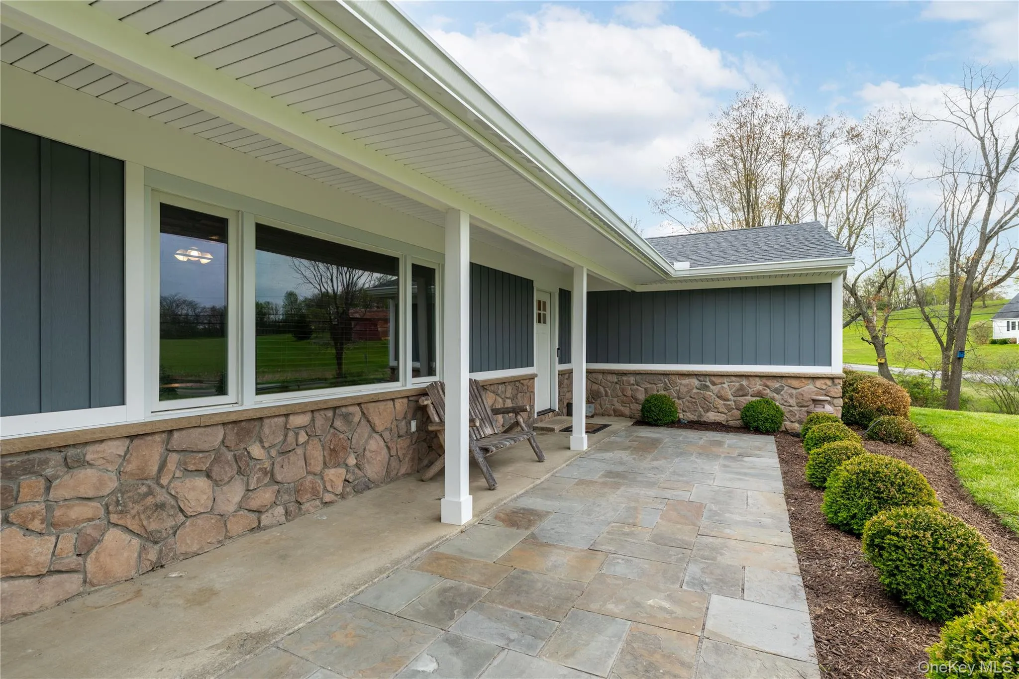 Stone and siding exterior featuring a covered patio with flagstone pavers, white columns, and a landscaped planting bed Stone and siding exterior featuring a covered patio with flagstone pavers, white columns, and a landscaped planting bed