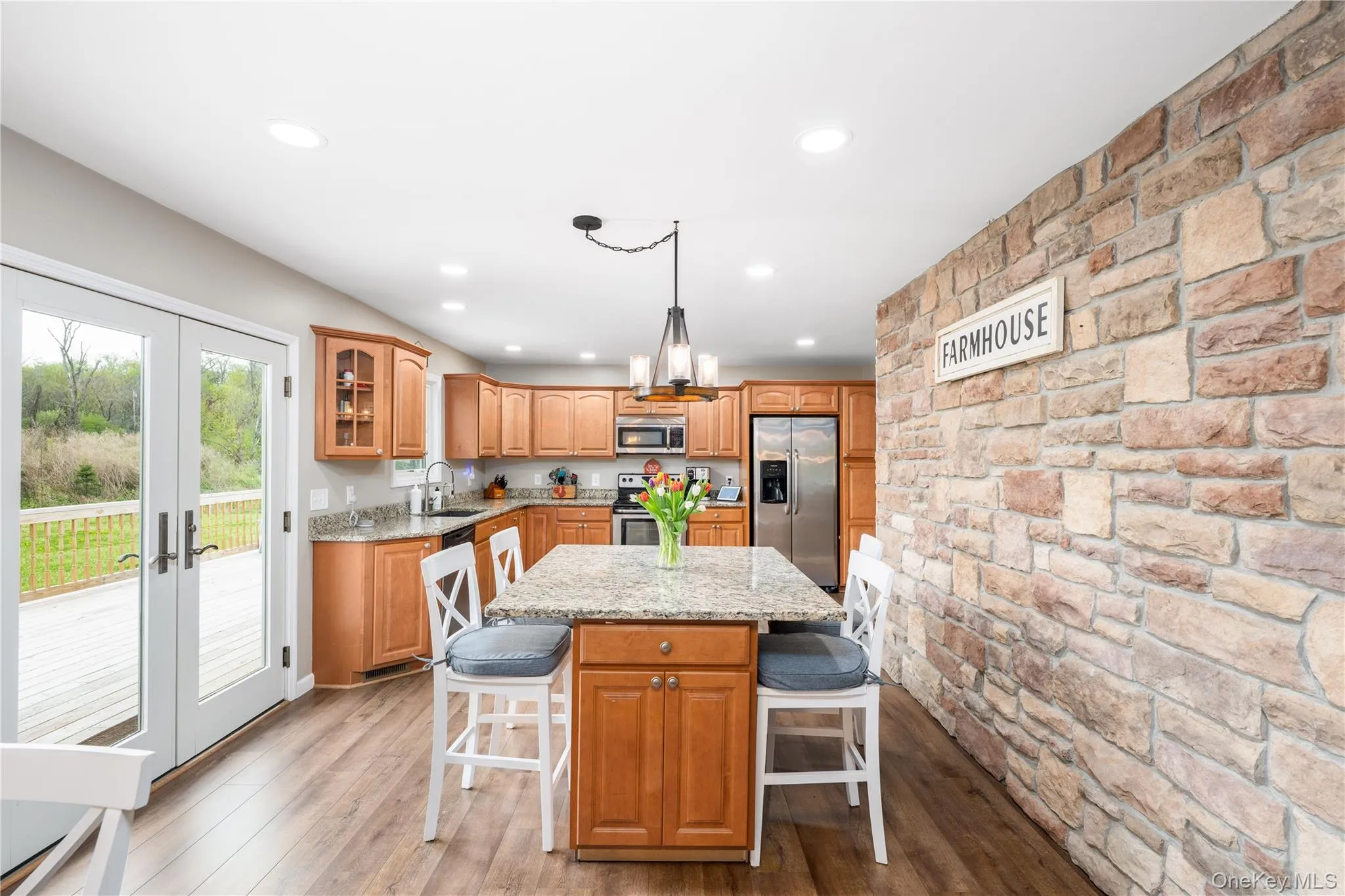 Open-concept kitchen featuring a stone accent wall, wood flooring, wood cabinetry, granite countertops, and French doors opening to a large single level deck Open-concept kitchen featuring a stone accent wall, wood flooring, wood cabinetry, granite countertops, and French doors opening to a large single level deck