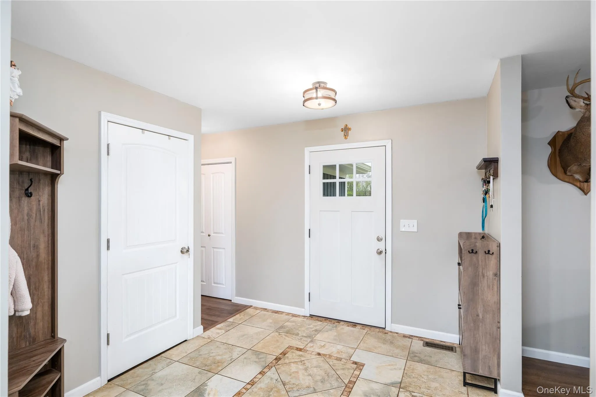 Entry foyer featuring ceramic tile flooring with decorative inlay, a white paneled door, and a white exterior door with window panes Entry foyer featuring ceramic tile flooring with decorative inlay, a white paneled door, and a white exterior door with window panes