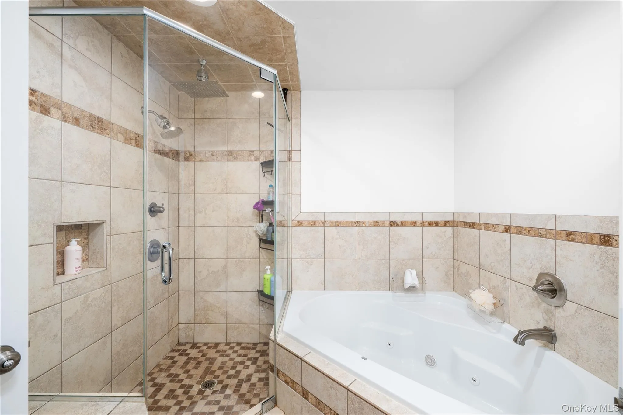 Ensuite bathroom featuring a corner jetted soaking tub, glass-enclosed shower, tiled walls, and a recessed shower niche Ensuite bathroom featuring a corner jetted soaking tub, glass-enclosed shower, tiled walls, and a recessed shower niche