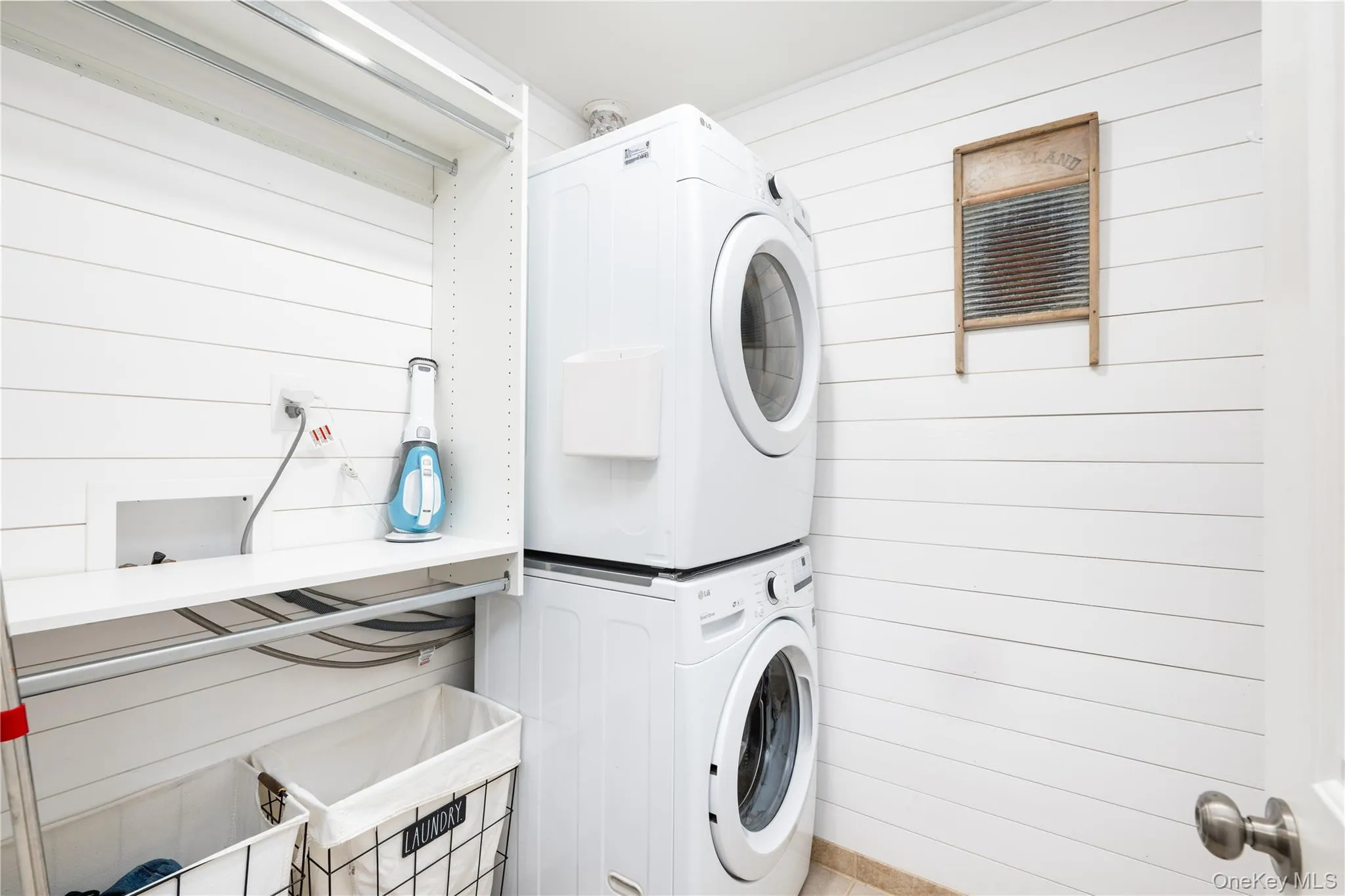 Main floor Laundry room featuring white shiplap walls, stacked washer and dryer, and a built-in shelving unit with hanging rods Main floor Laundry room featuring white shiplap walls, stacked washer and dryer, and a built-in shelving unit with hanging rods