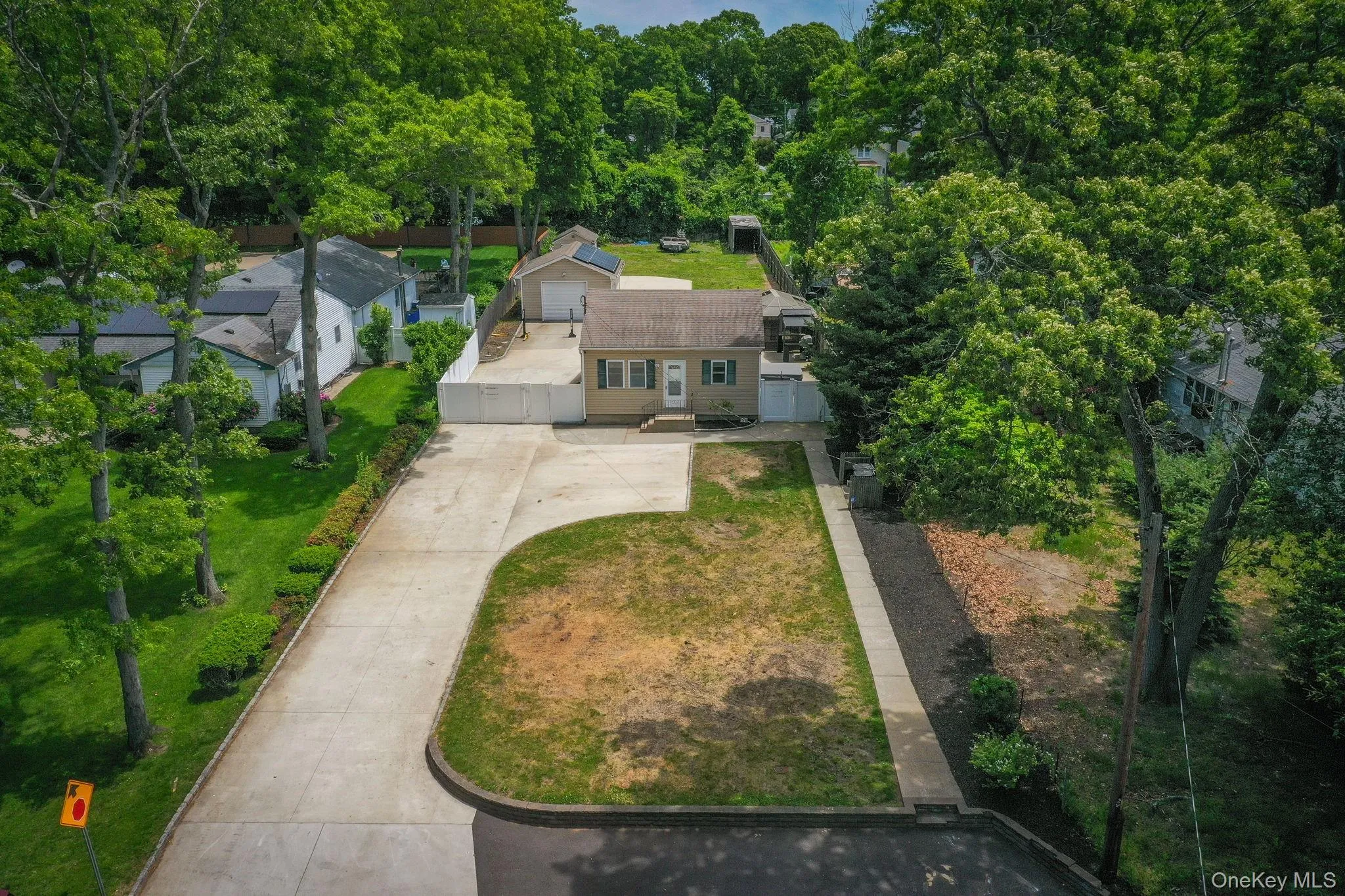 Single-story residence featuring a paved driveway, front lawn, and mature trees Single-story residence featuring a paved driveway, front lawn, and mature trees
