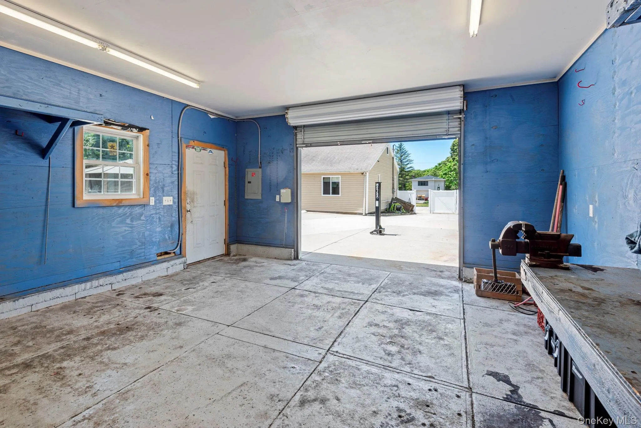 Garage interior featuring a roll-up door, fluorescent lighting, a side window, and an interior access door Garage interior featuring a roll-up door, fluorescent lighting, a side window, and an interior access door
