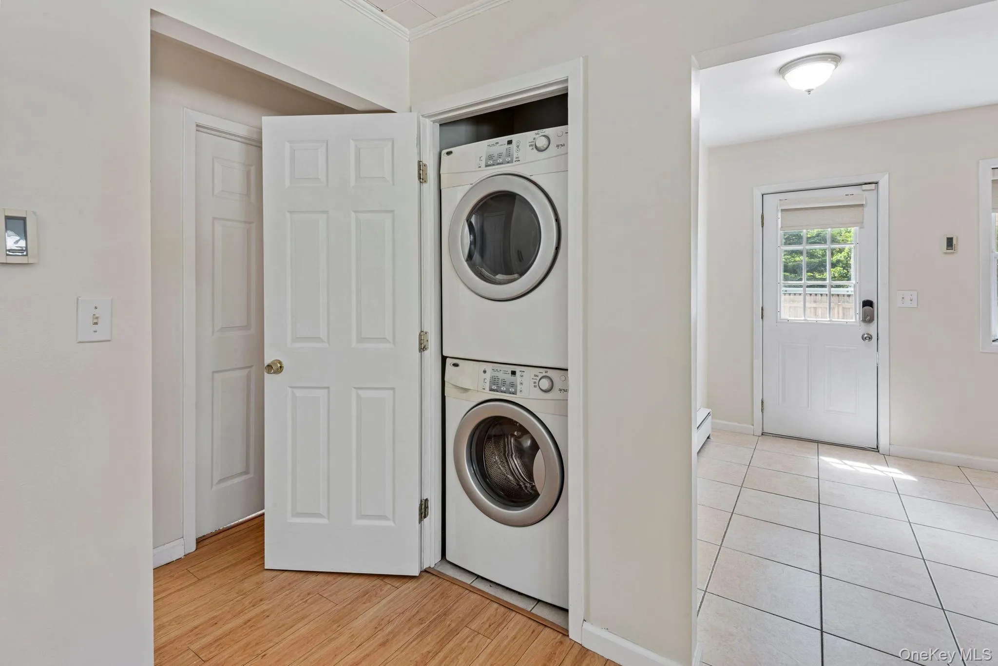 Laundry closet featuring a stacked washer and dryer off the kitchen / living room area with hardwood floors Laundry closet featuring a stacked washer and dryer off the kitchen / living room area with hardwood floors
